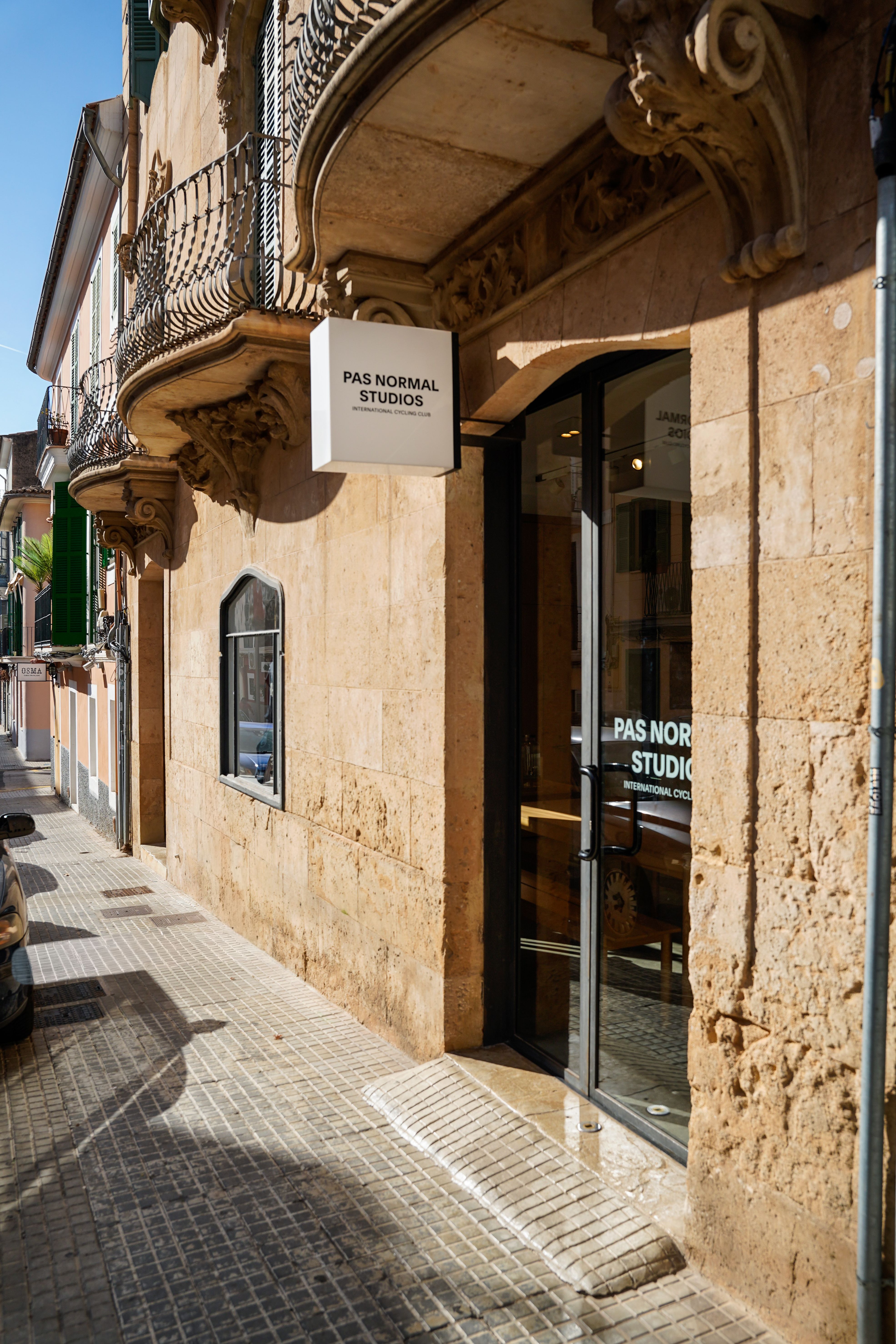 Storefront exterior with stone facade, ornate balcony, and glass entrance on cobblestone street in Palma