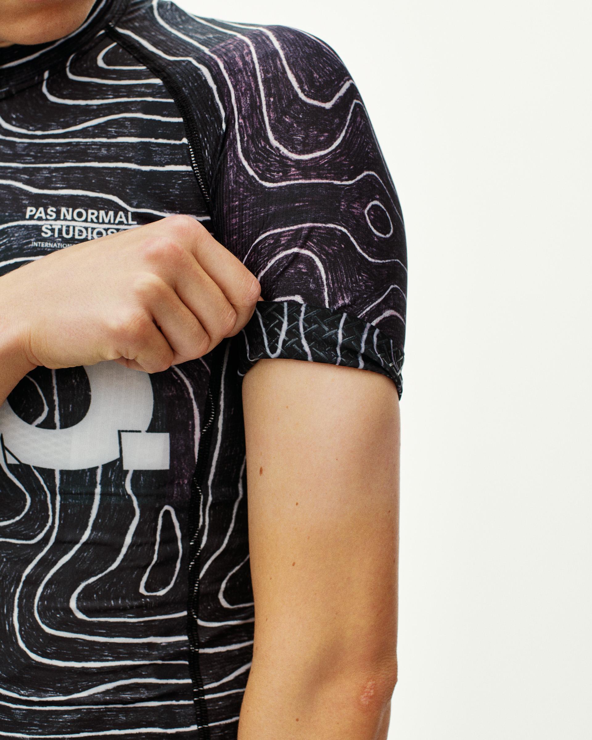 Black T.K.O. Mechanism women's cycling jersey, side detail on model with topographic allover print and contrast sleeve cuff