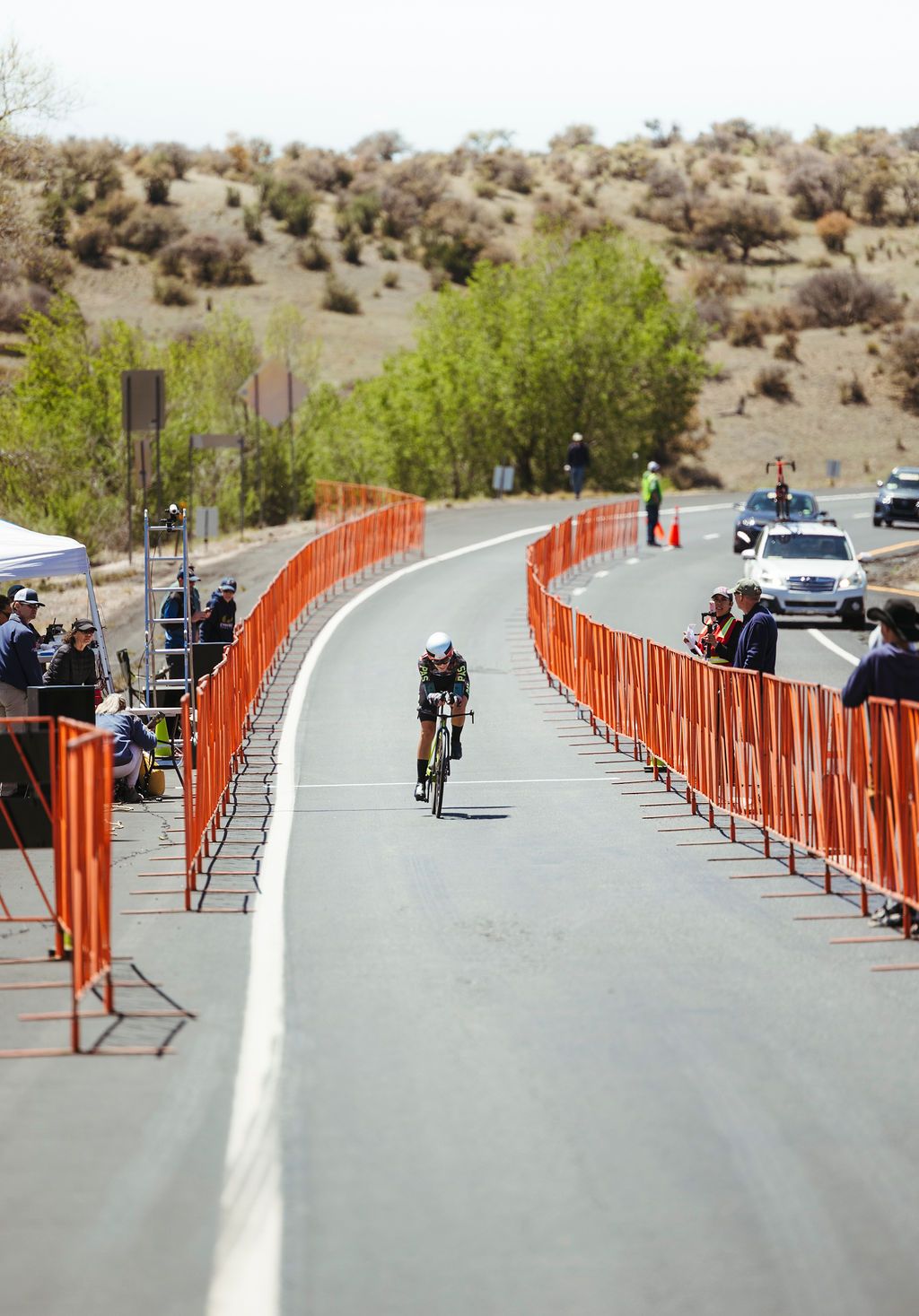 Cyclist racing on closed road during time trial with orange barriers and spectators