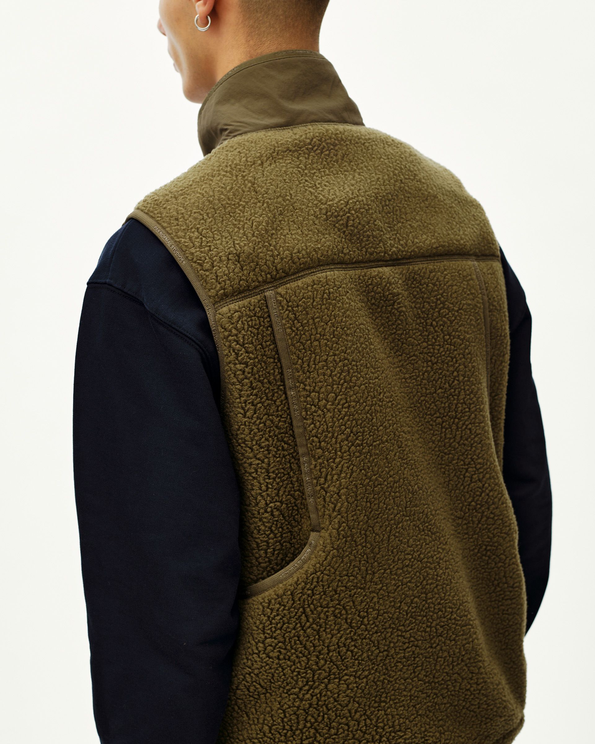 Deep Olive Off-Race Pile Fleece vest on model, rear three-quarter view with vertical back zip pocket