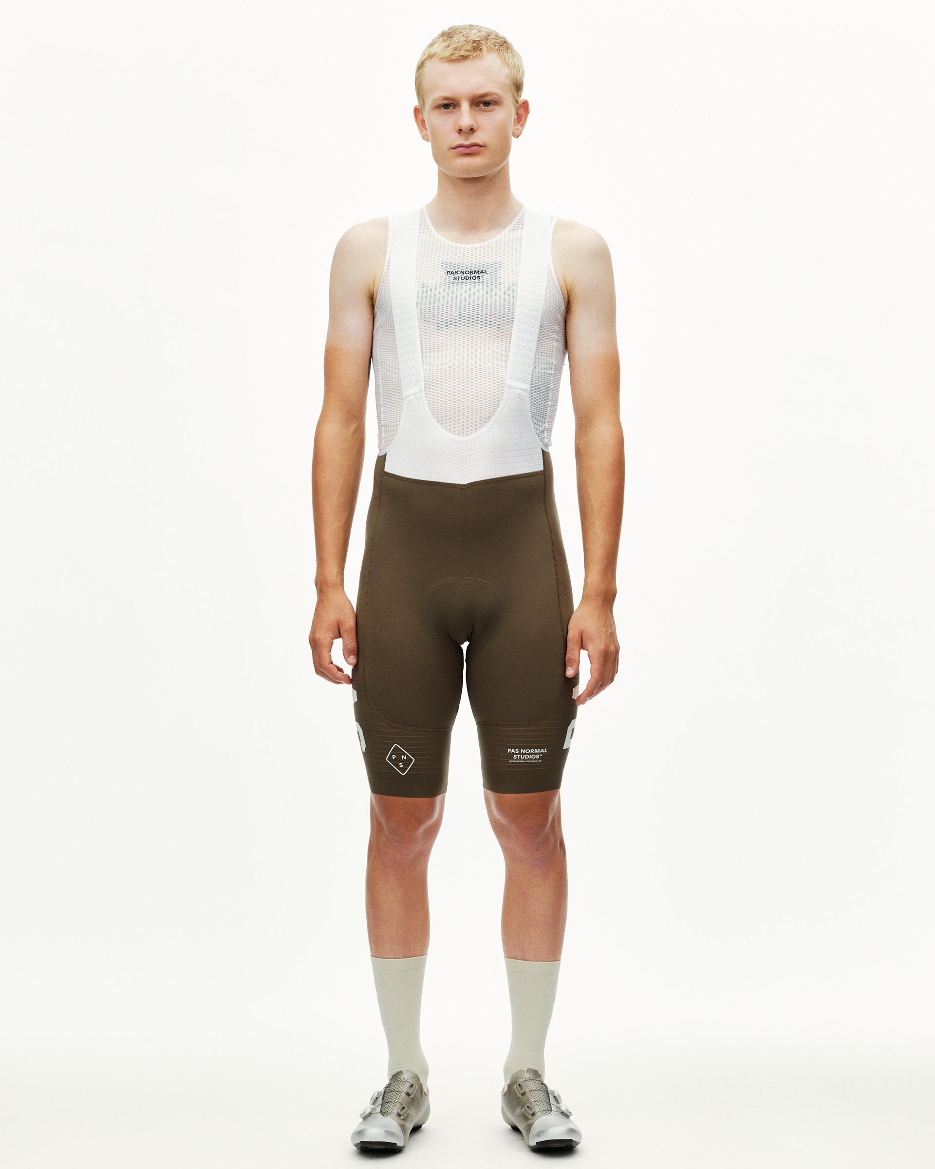 Dark Earth brown PAS Mechanism Pro cycling bibs on model, front view with white mesh bib straps and leg logo print