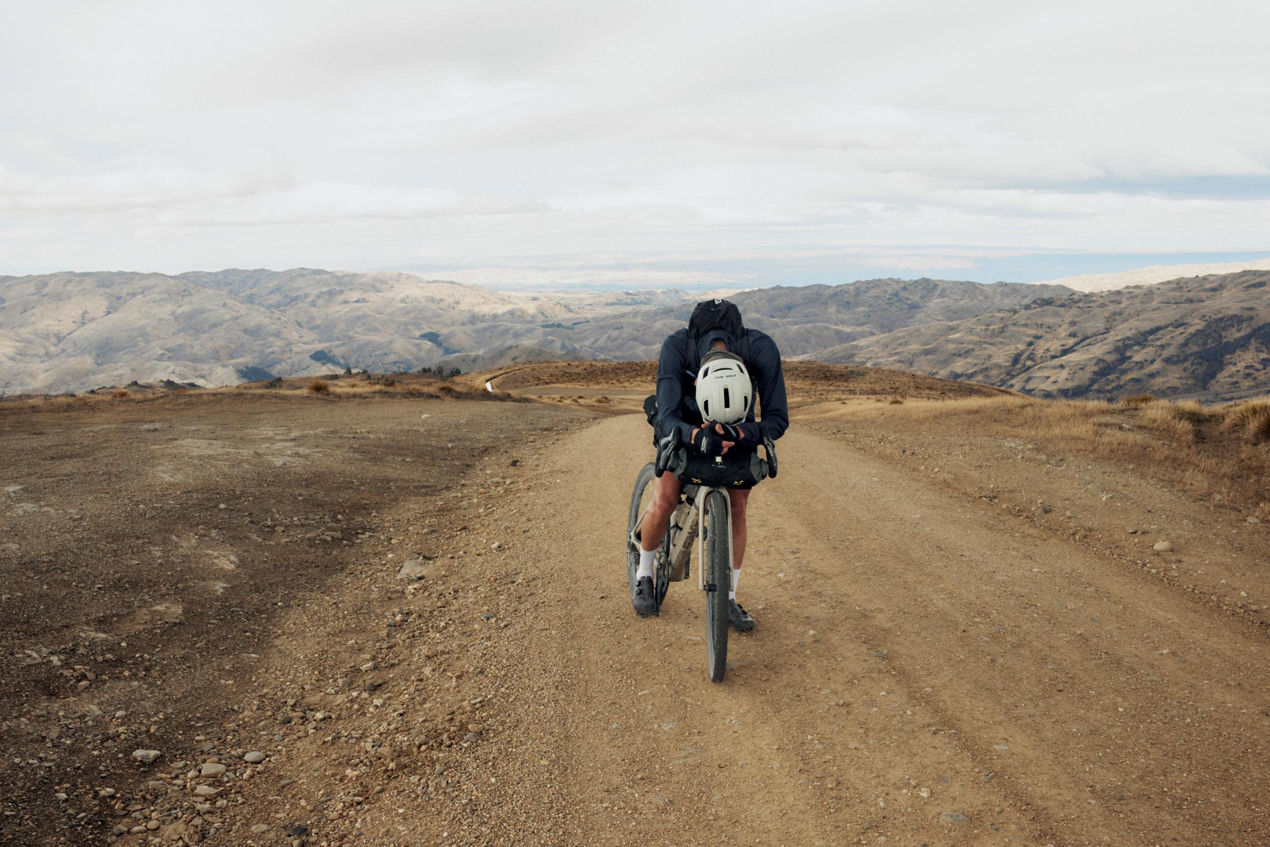 Cyclist on gravel bike riding dirt road through mountainous desert landscape