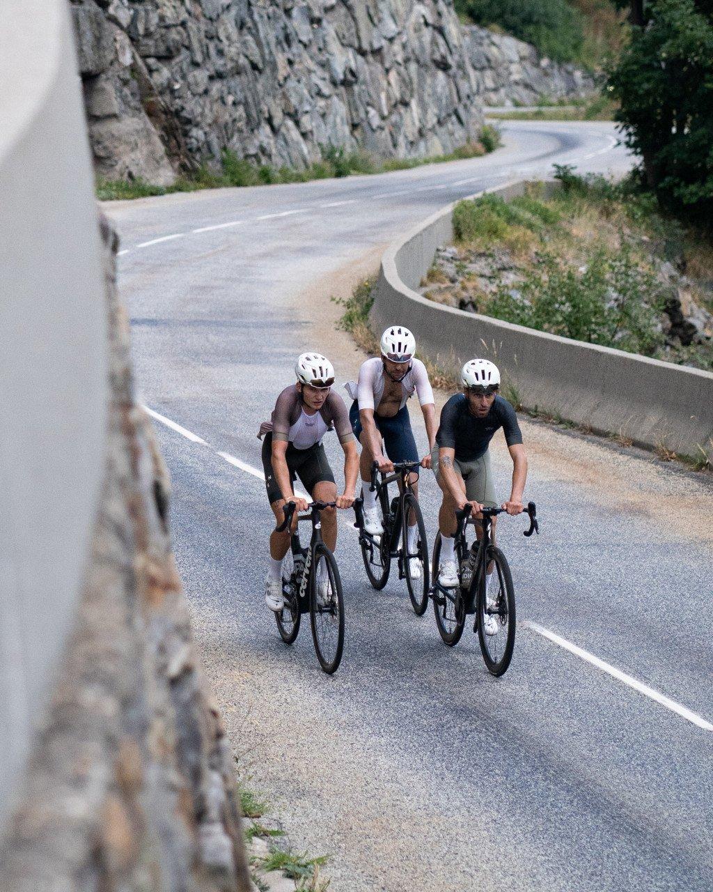 Three cyclists in aerodynamic position riding time trial bikes on winding mountain road