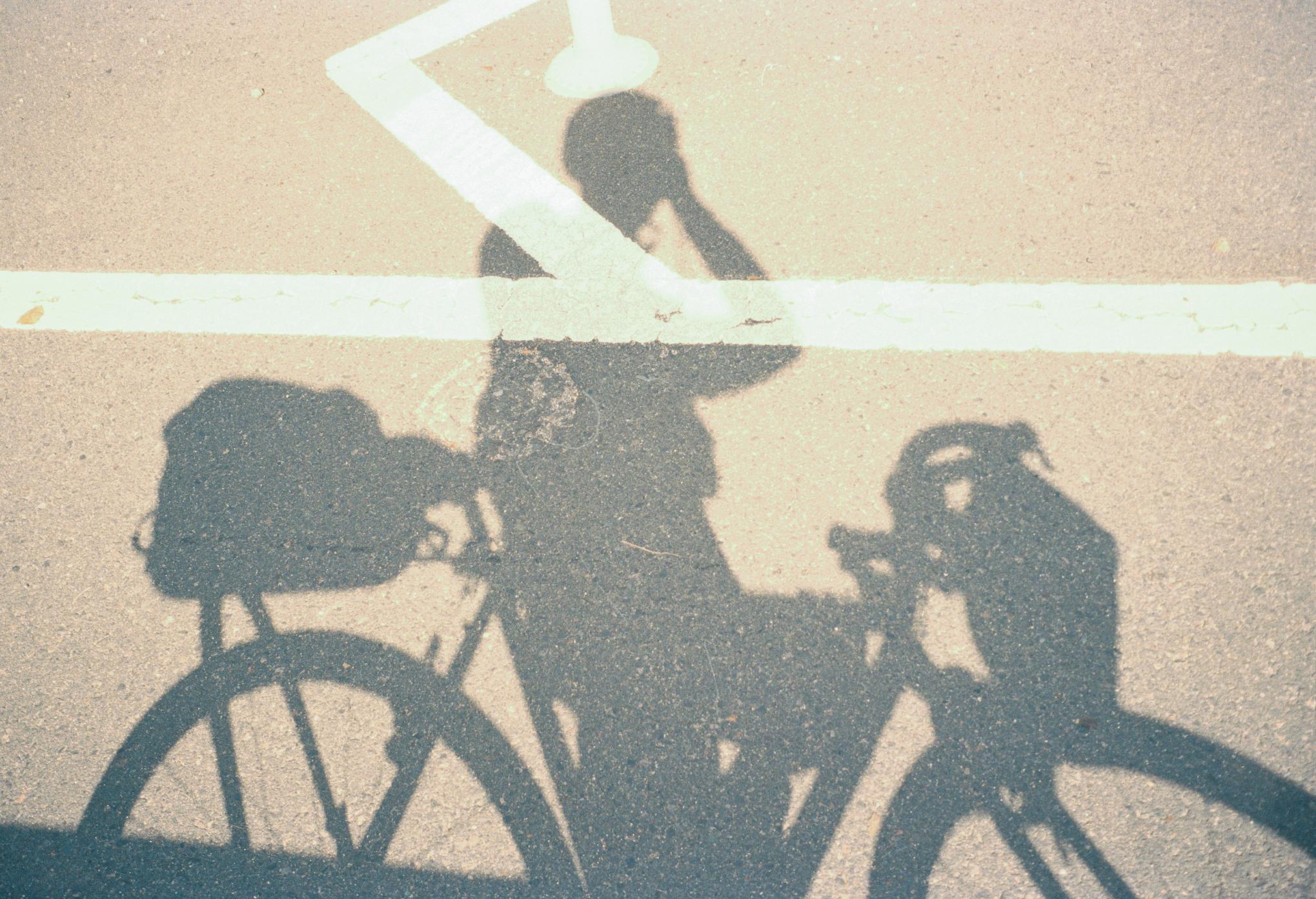 Shadow of cyclist and bicycle cast on concrete surface with white road markings