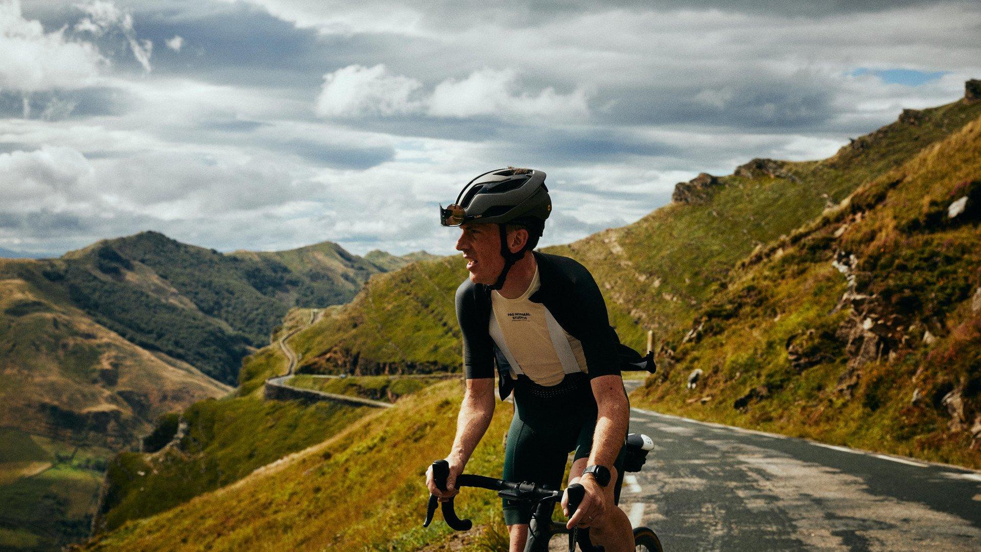 Model wearing black long-sleeve cycling jersey with tan chest panel in mountain landscape