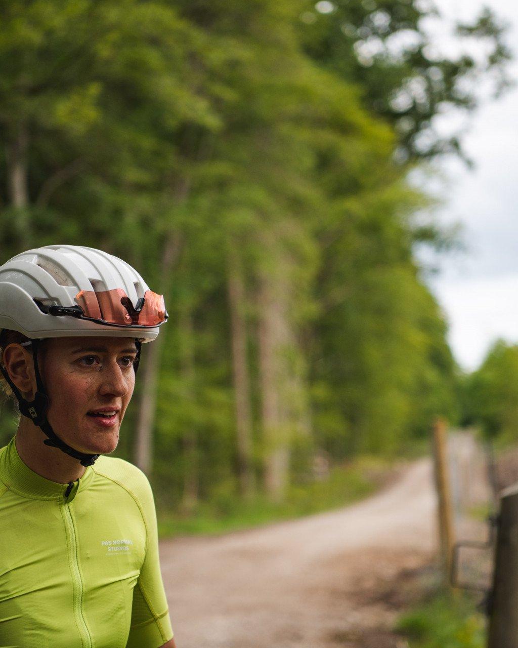 Model wearing green long-sleeve cycling jersey with white helmet outdoors on tree-lined path