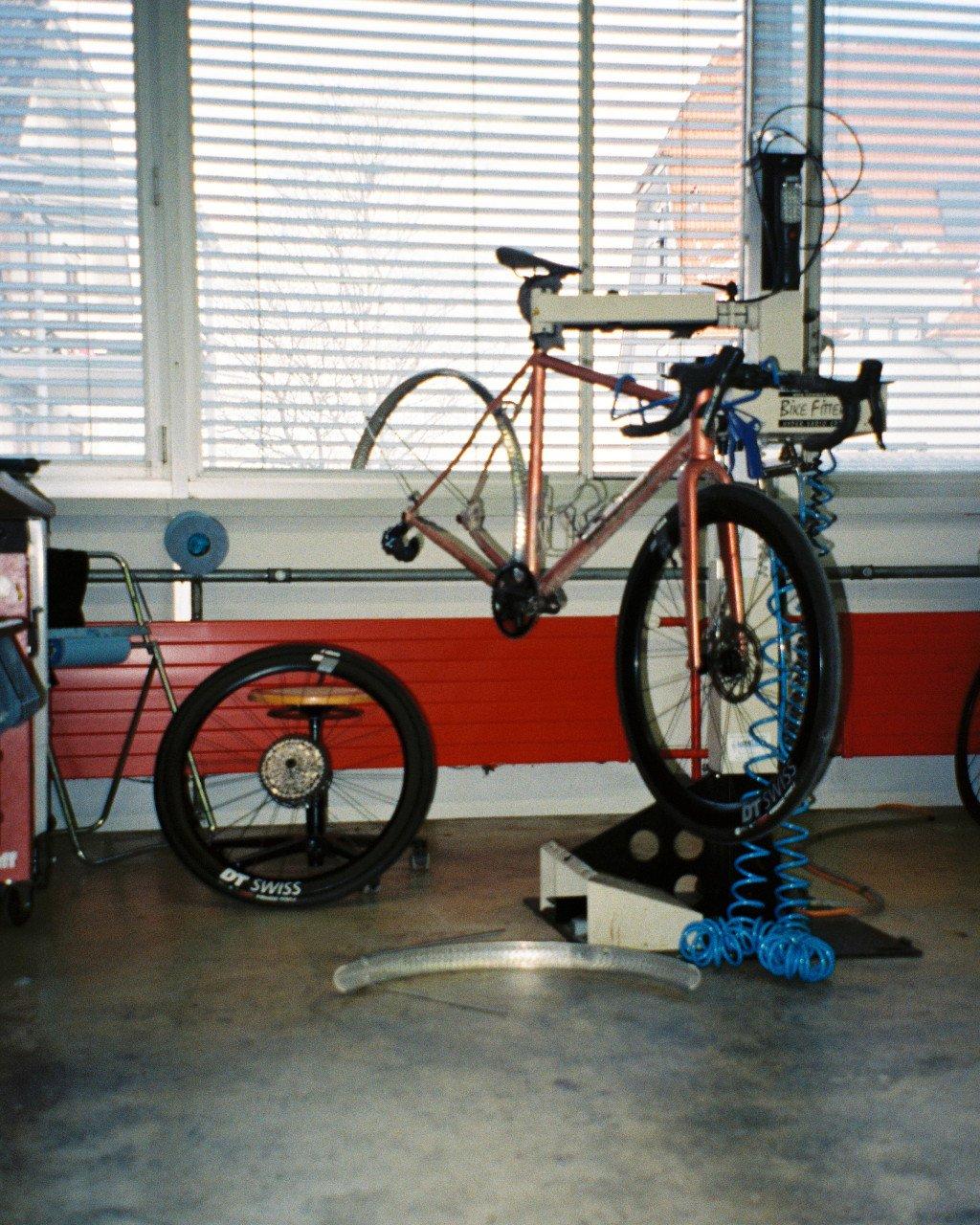 Copper-colored road bike on indoor trainer in windowed room with venetian blinds
