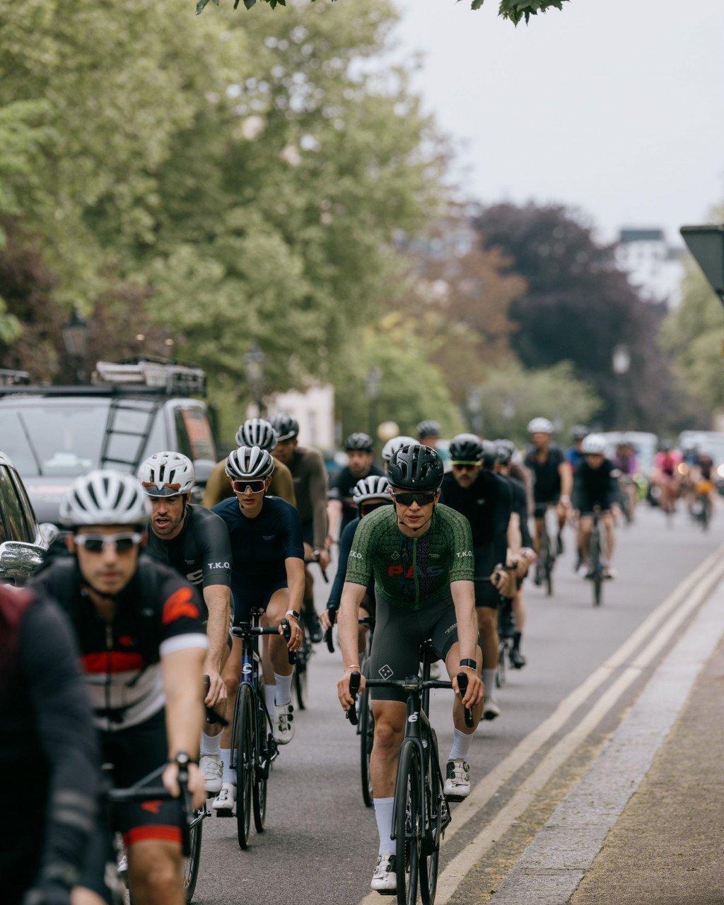 Cyclists in premium cycling apparel riding time trial bikes on tree-lined road