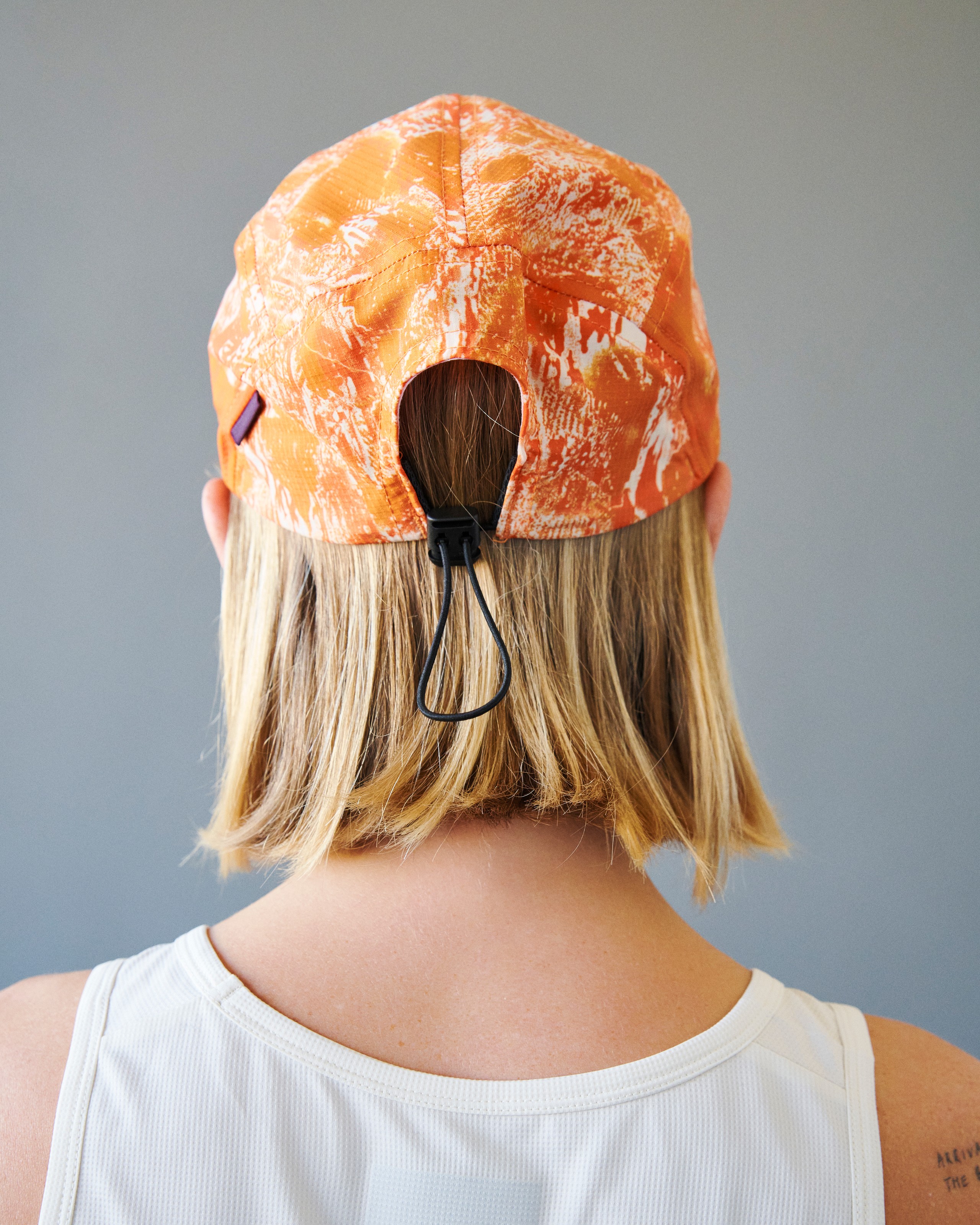 Orange Balance cycling cap on model, rear view with all-over white splash print and black toggle closure