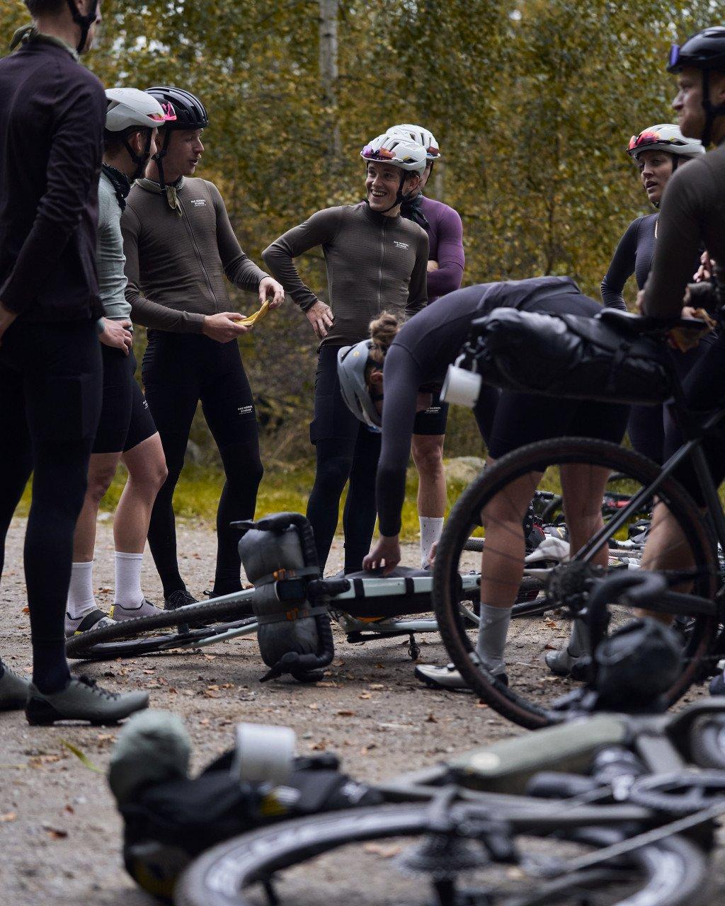 Cyclists in dark cycling apparel gathered around bikes during roadside stop in autumn forest