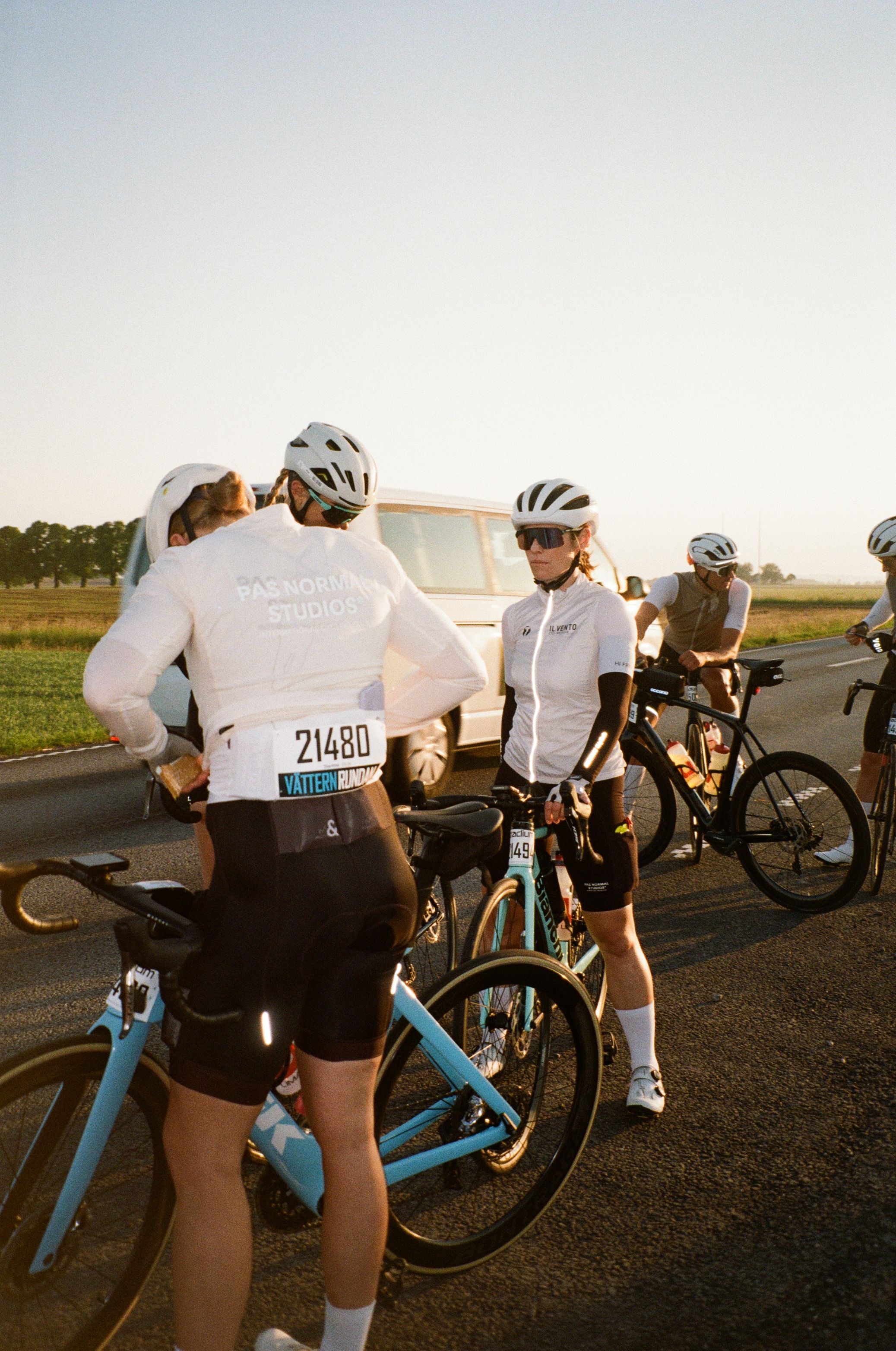 Cyclists in white jerseys with logo branding preparing at roadside during Vätternrundan race