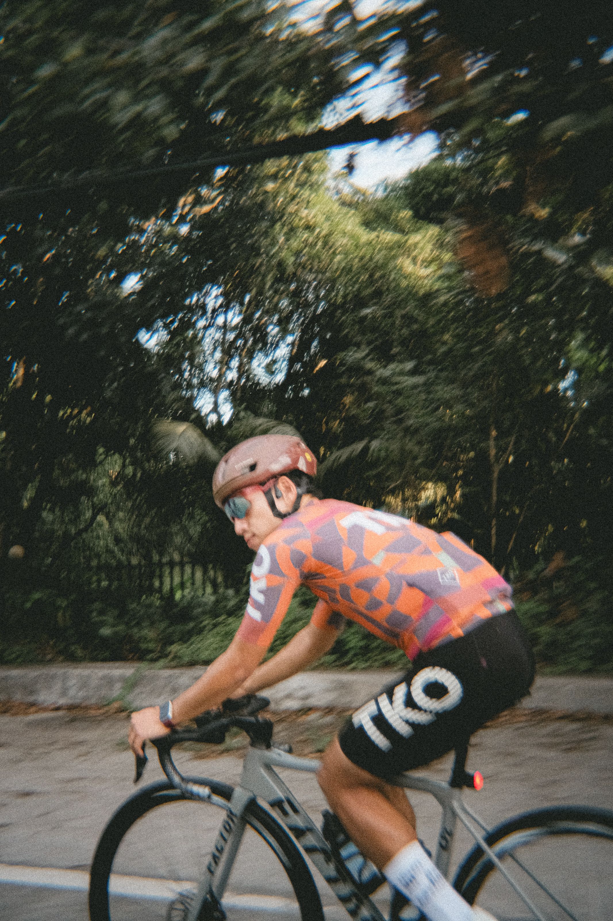 Cyclist wearing colorful geometric pattern jersey and black shorts riding on tree-lined road