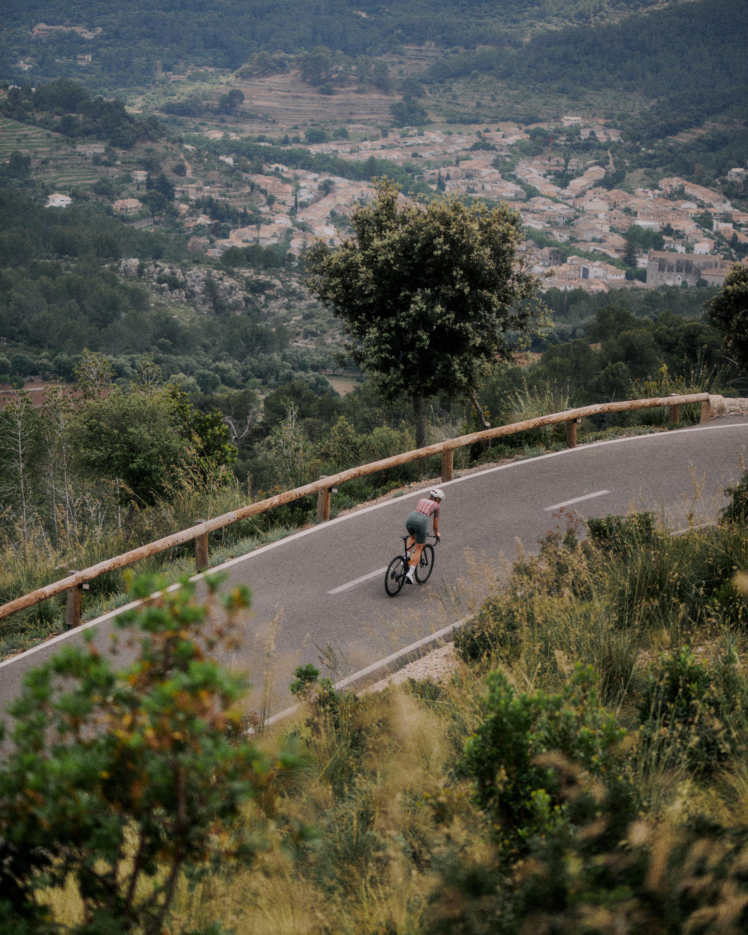 Cyclist in pink jersey descending winding mountain road through Mediterranean hillside landscape