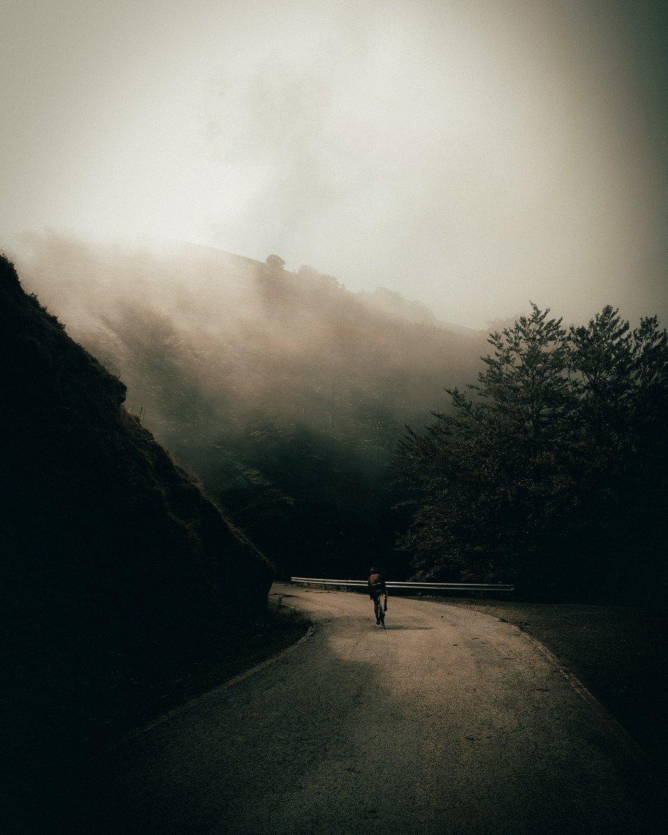 Cyclist on misty mountain road surrounded by fog-covered hills and trees