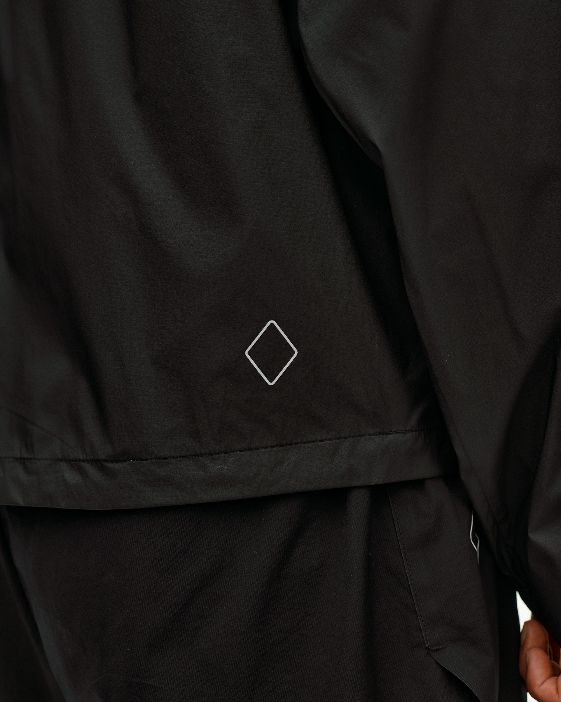 Dusty Earth black Balance Windproof jacket, detail on model showing diamond logo at hem