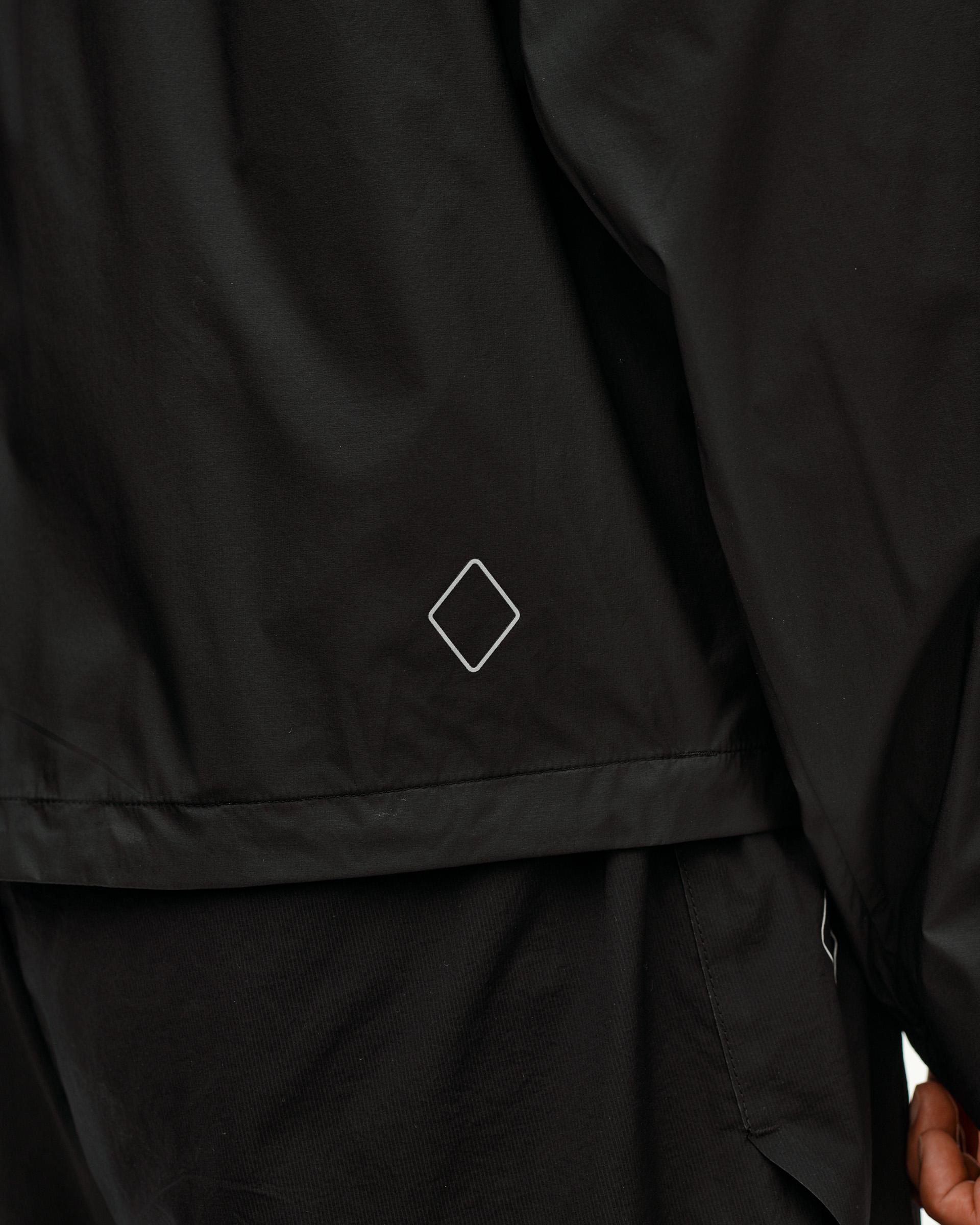 Dusty Earth black Balance Windproof jacket, detail on model showing diamond logo at hem