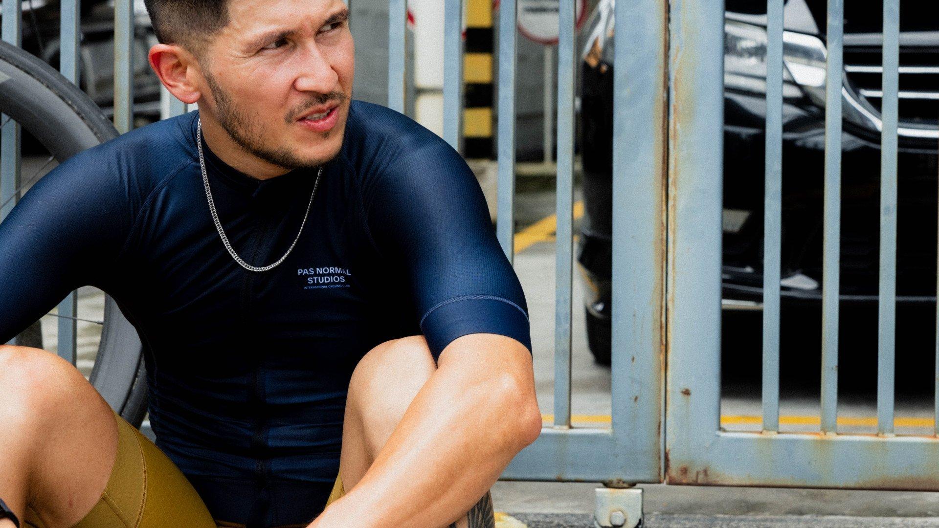 Model wearing navy blue short sleeve jersey with chest branding, sitting in urban setting