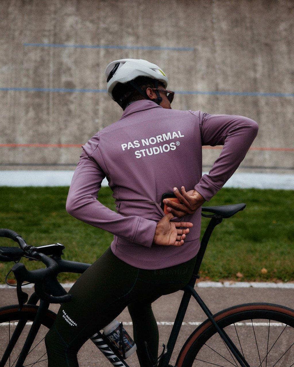 Model wearing purple long-sleeve cycling jersey with back branding, shown with bike in urban setting