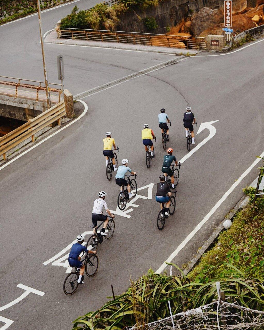 Group of cyclists in colorful jerseys riding up winding mountain road with directional arrows