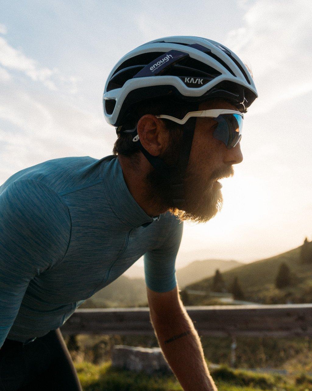 Model wearing blue textured cycling jersey in aerodynamic position outdoors at sunset