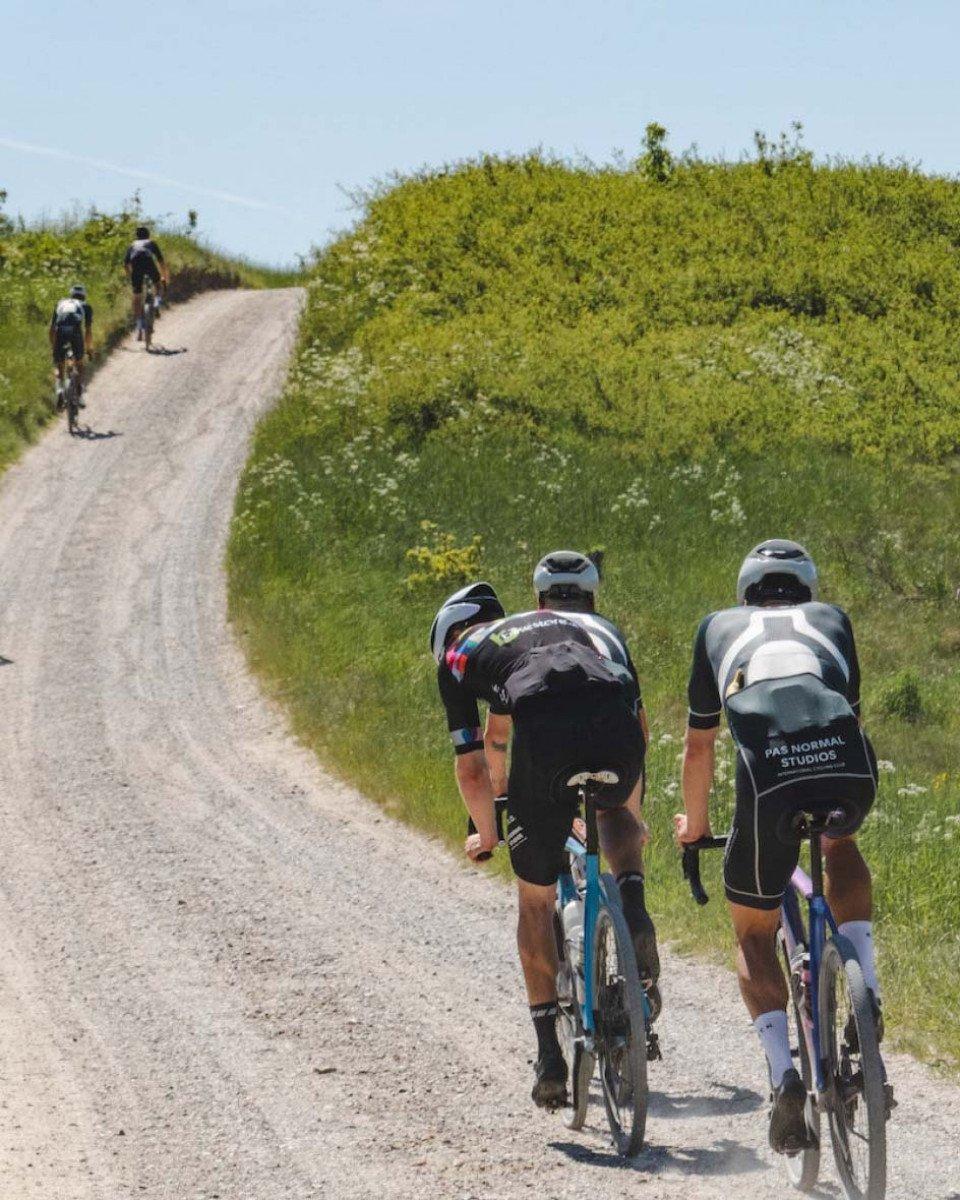 Cyclists in aero position riding uphill on gravel road through green countryside