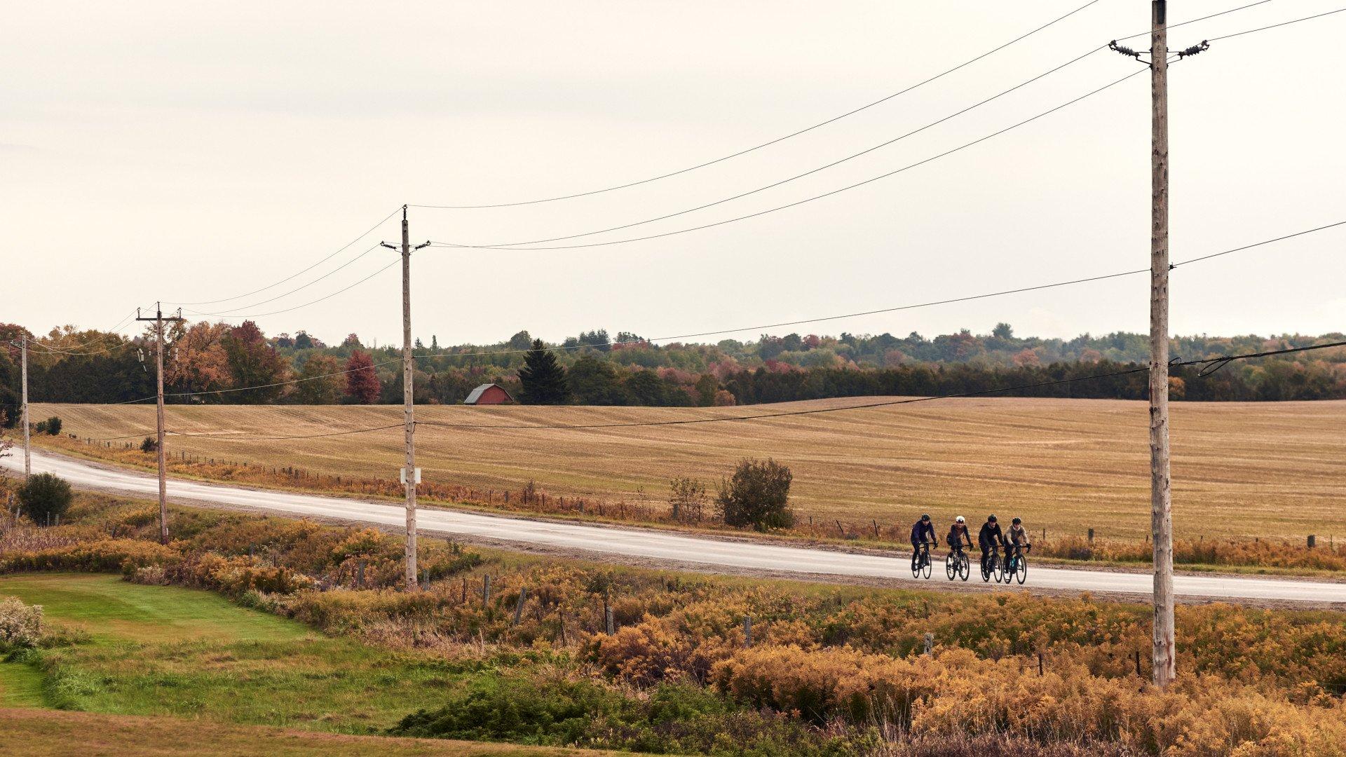 Four cyclists riding on rural road through autumn countryside with fields and power lines
