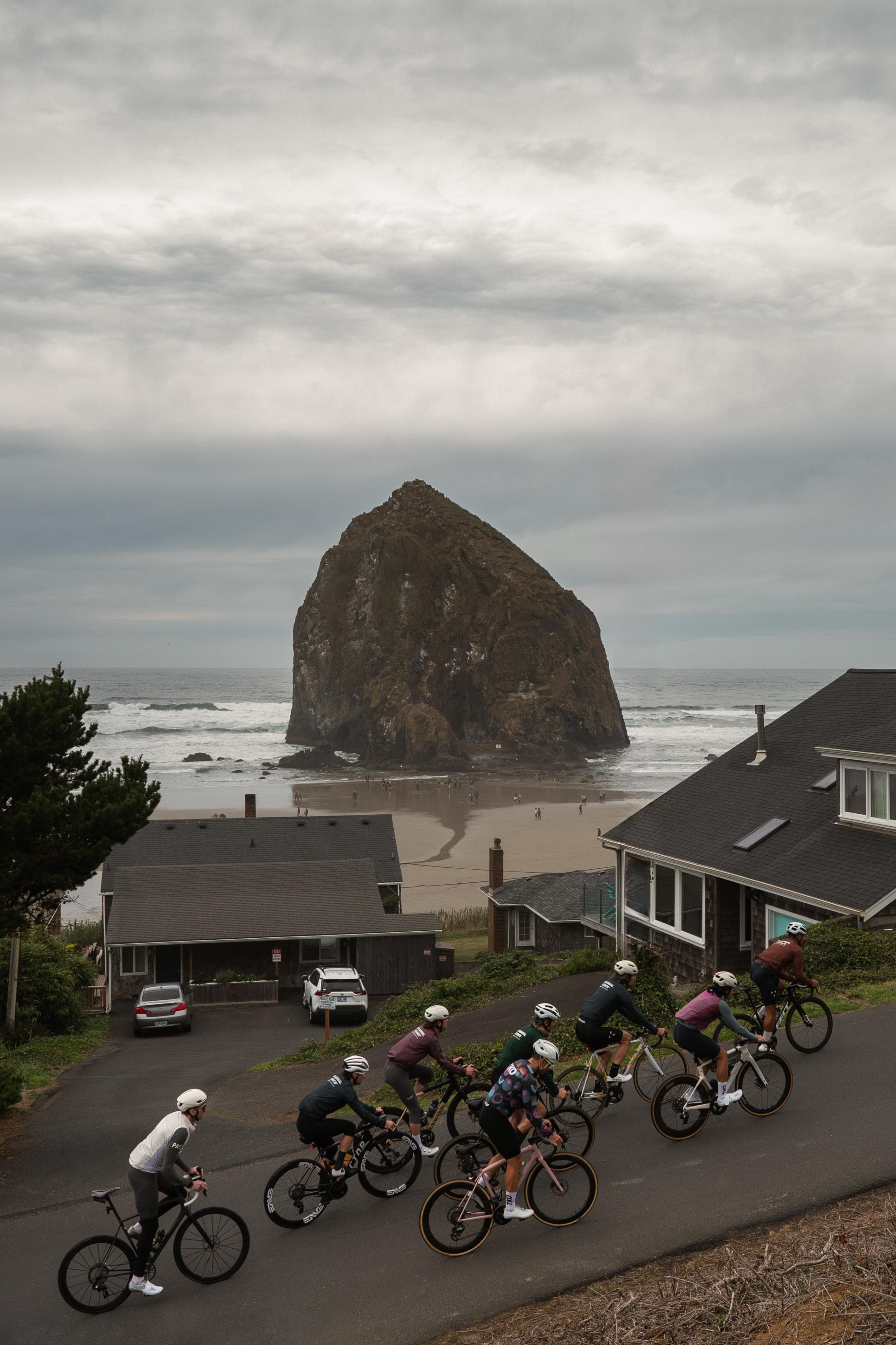 Group of cyclists in colorful jerseys riding on coastal road with large rock formation and ocean backdrop