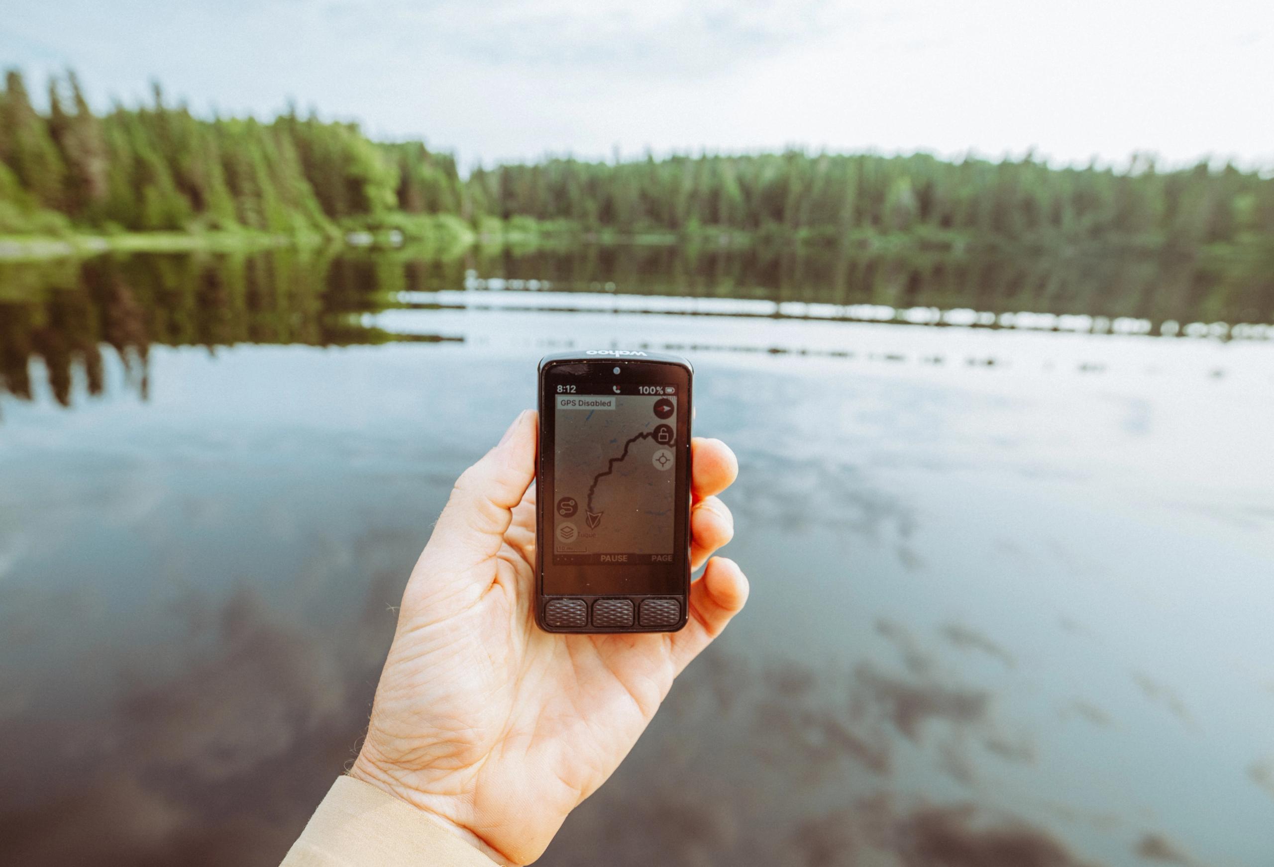 Hand holding smartphone displaying GPS cycling route map by lake with forest reflection