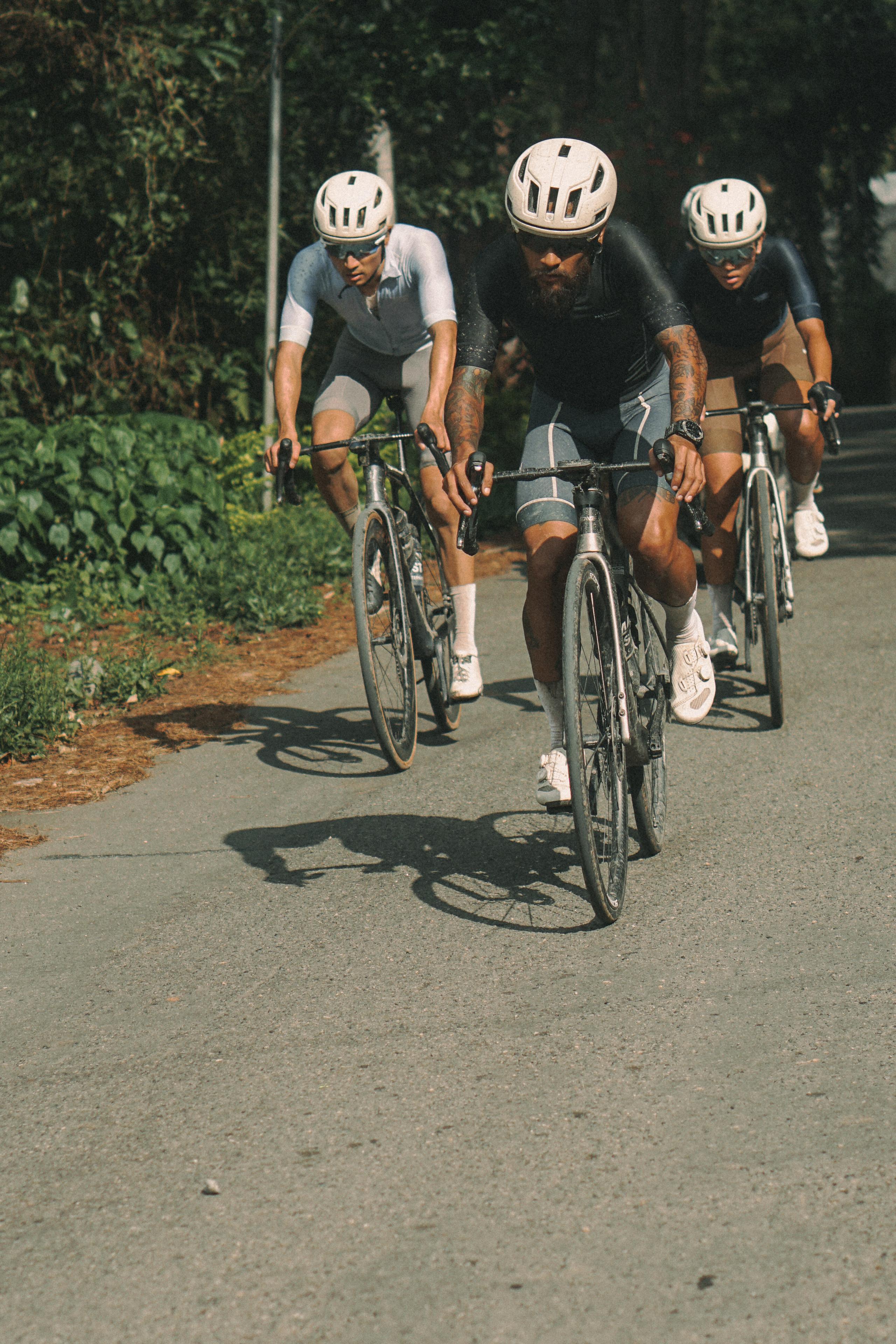 Three cyclists in aerodynamic position on time trial bikes wearing helmets and cycling apparel on road