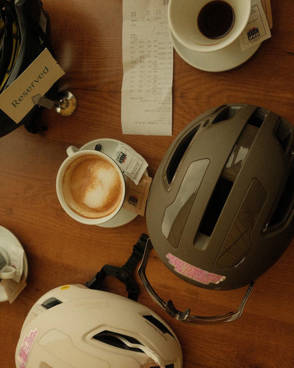 Cycling helmets and coffee cup on wooden table with receipt and reservation card