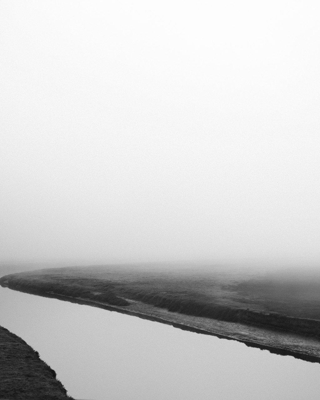Black and white landscape showing misty coastline with winding road through rolling hills