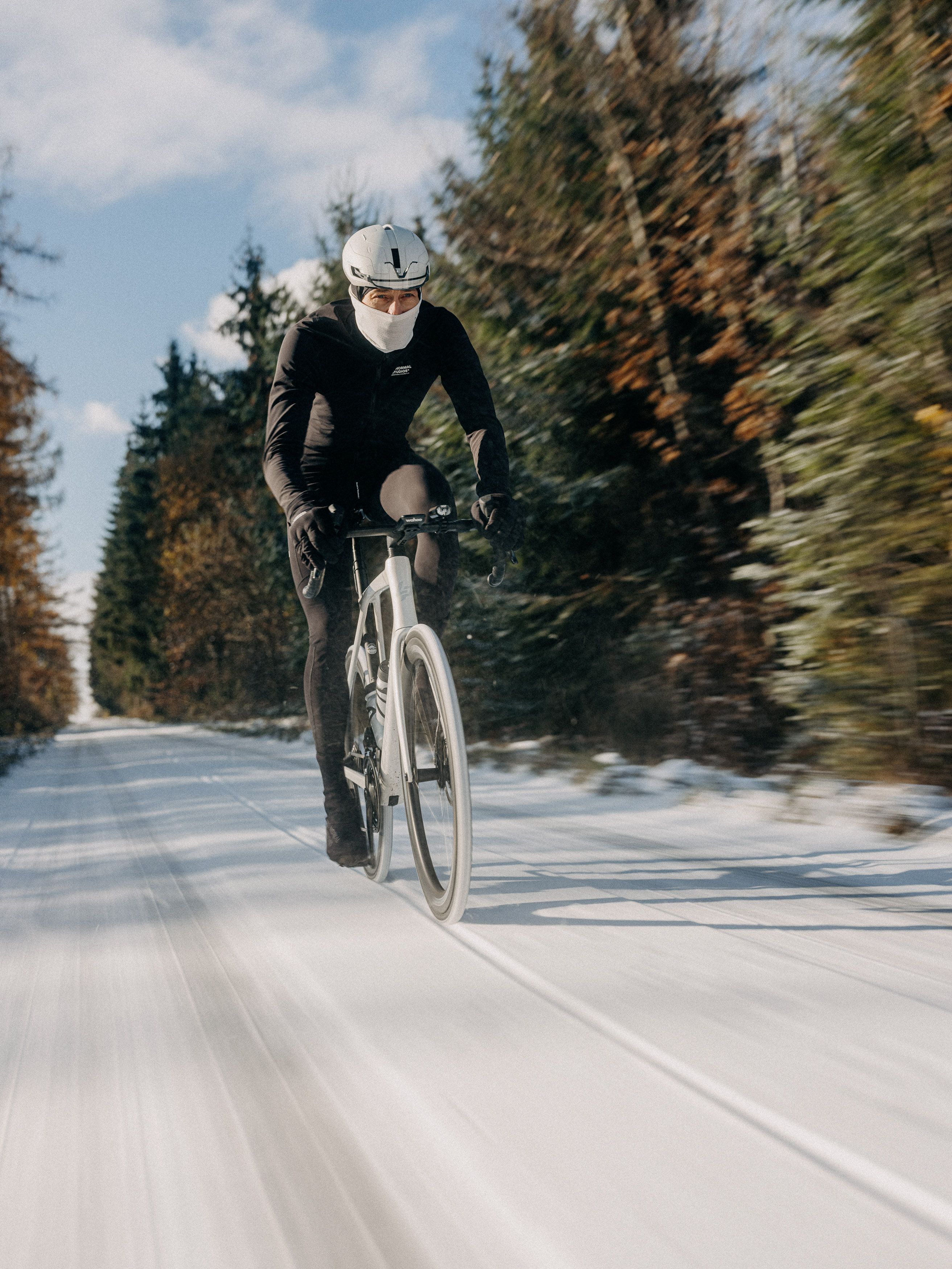 Model wearing black cycling apparel on time trial bike in snowy winter landscape