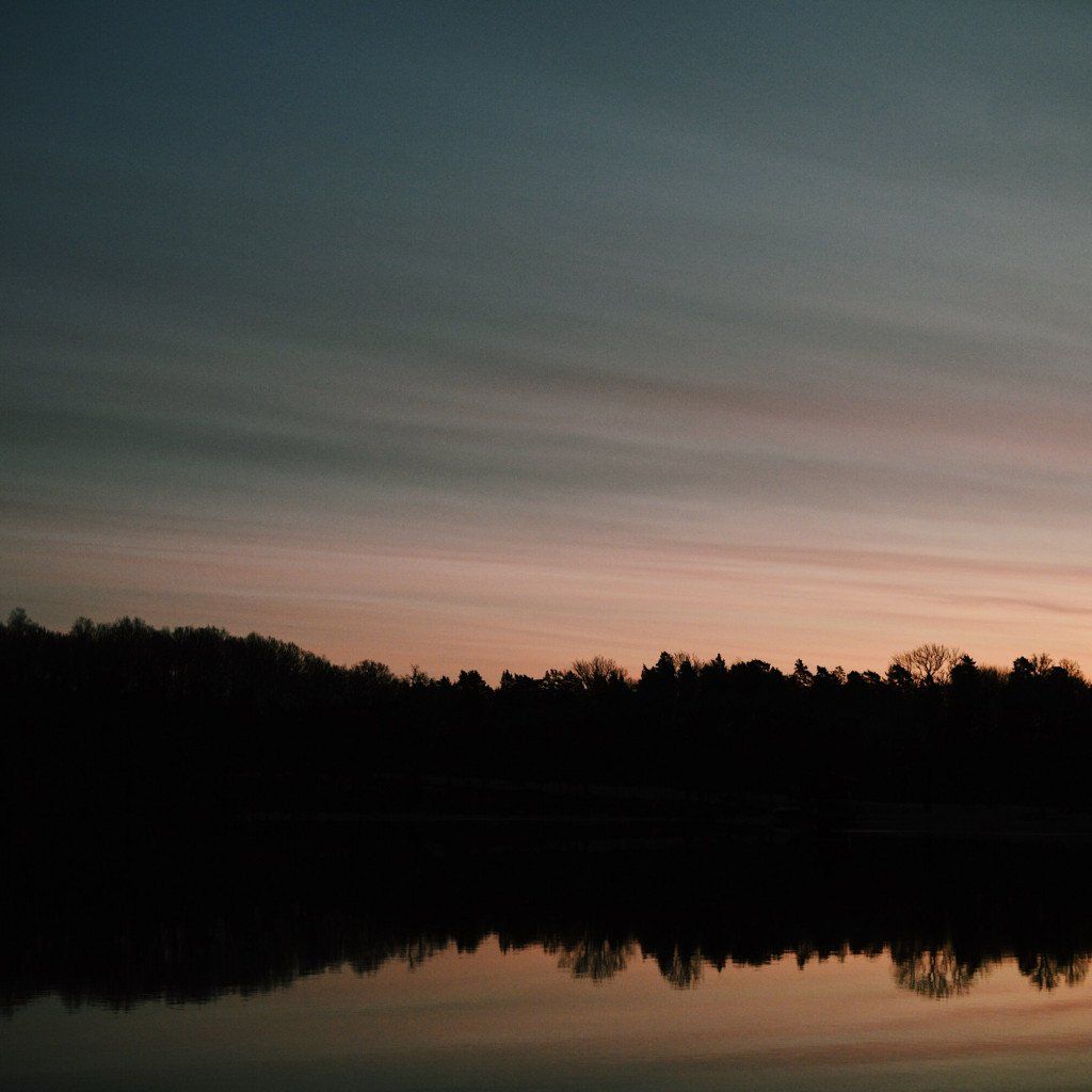 Sunset over lake with treeline silhouette and cloudy sky reflection