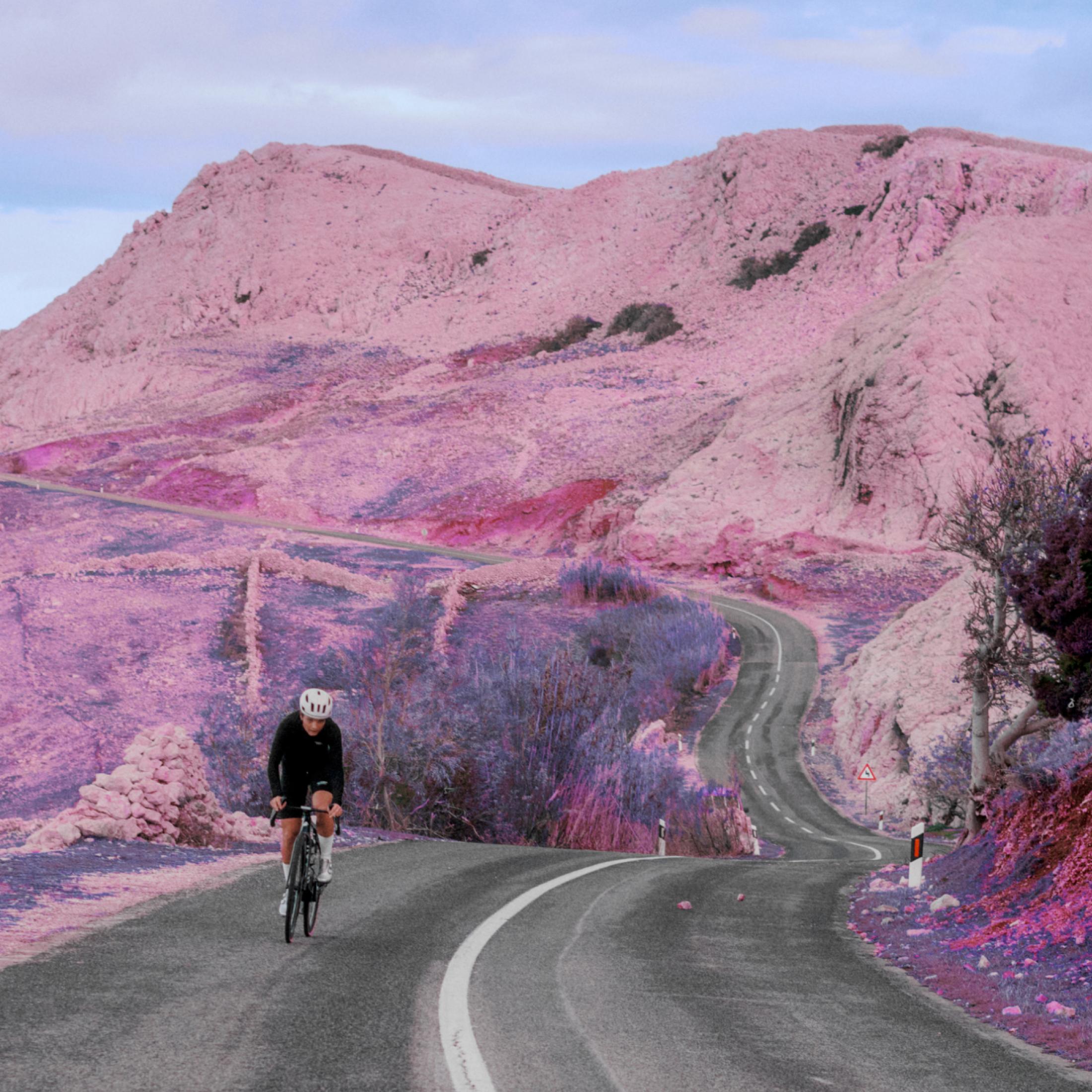 Cyclist on winding mountain road through pink-toned desert landscape