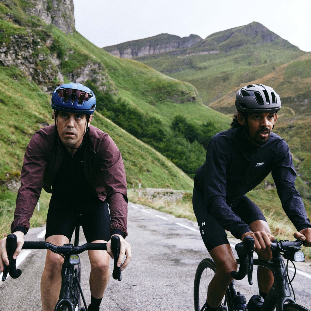 Two cyclists in aero position on mountain road wearing burgundy and navy long sleeve jerseys with helmets