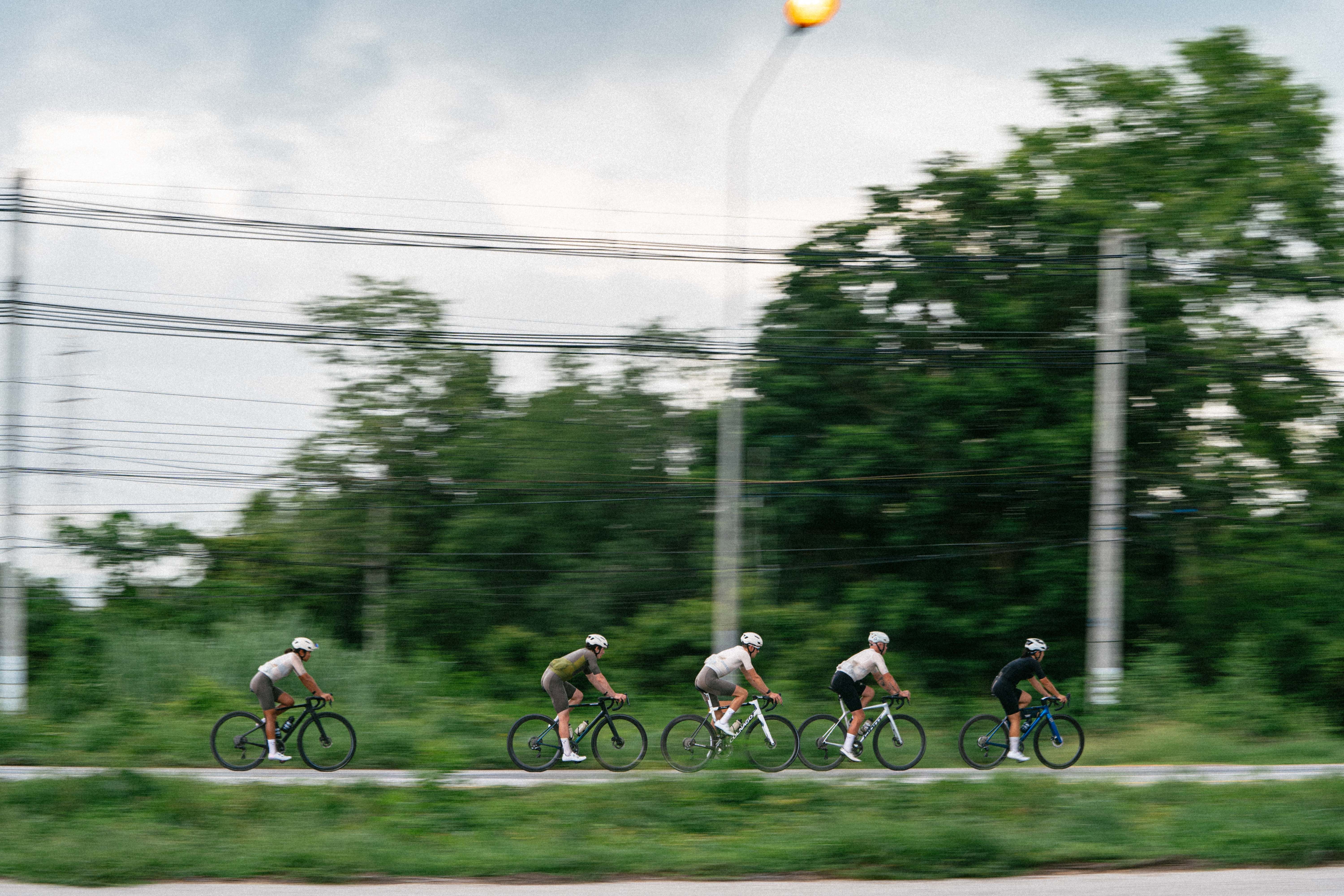 Five cyclists in aerodynamic position riding time trial bikes on rural road with green landscape