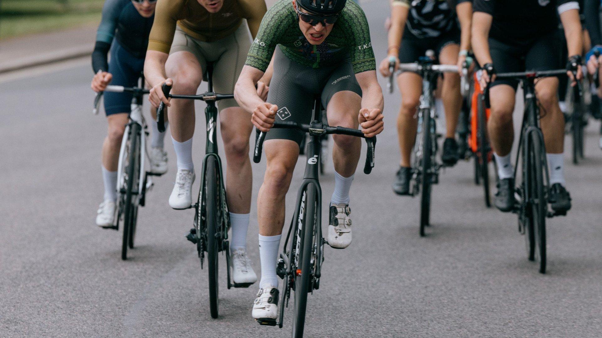 Cyclists in aerodynamic position racing on road, featuring green textured cycling kit in foreground