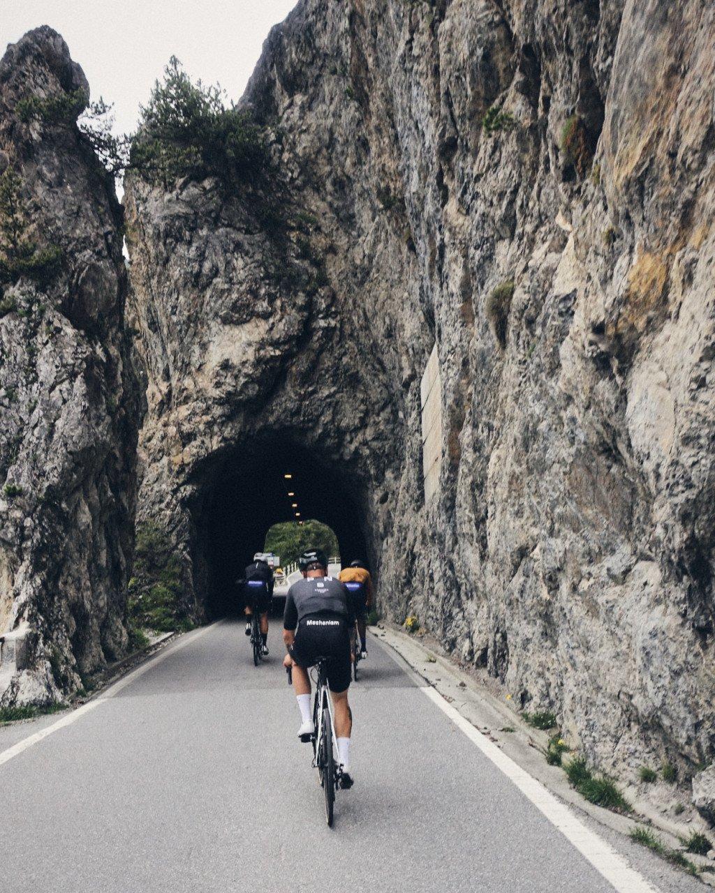 Cyclists riding through stone tunnel on mountain road with rocky cliff walls