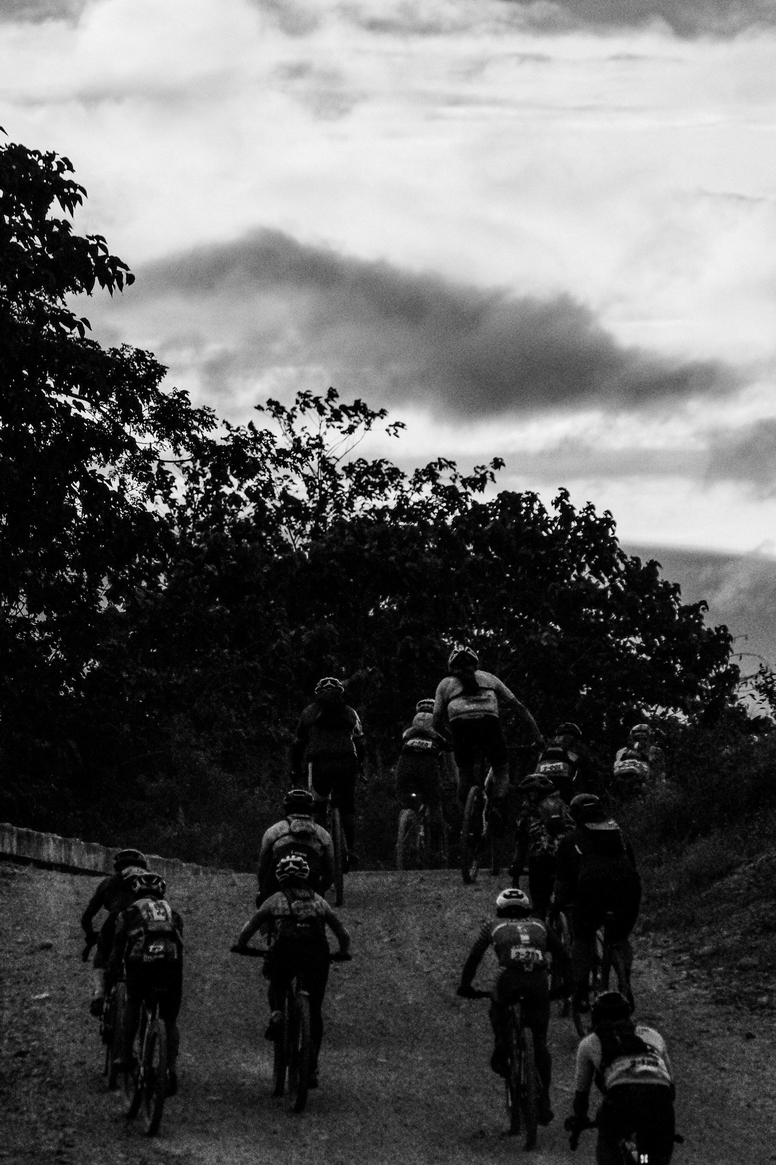 Group of cyclists racing on gravel road through hilly terrain in black and white