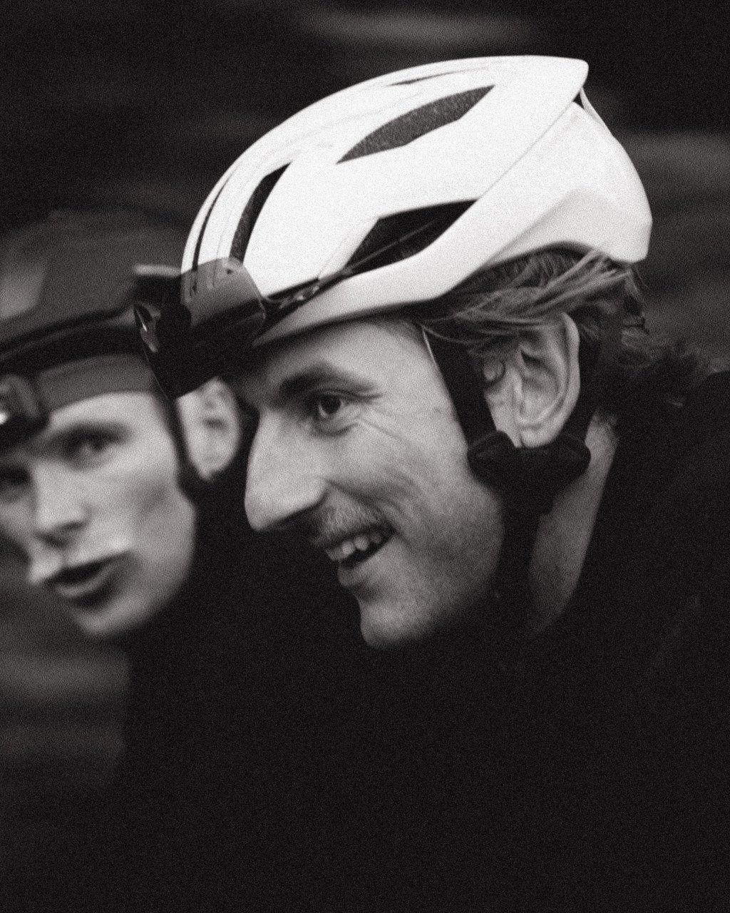Two cyclists wearing white cycling helmets in black and white photograph