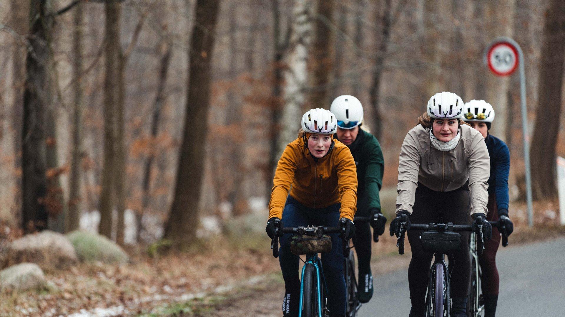 Cyclists in winter cycling apparel riding time trial bikes on forest road in autumn