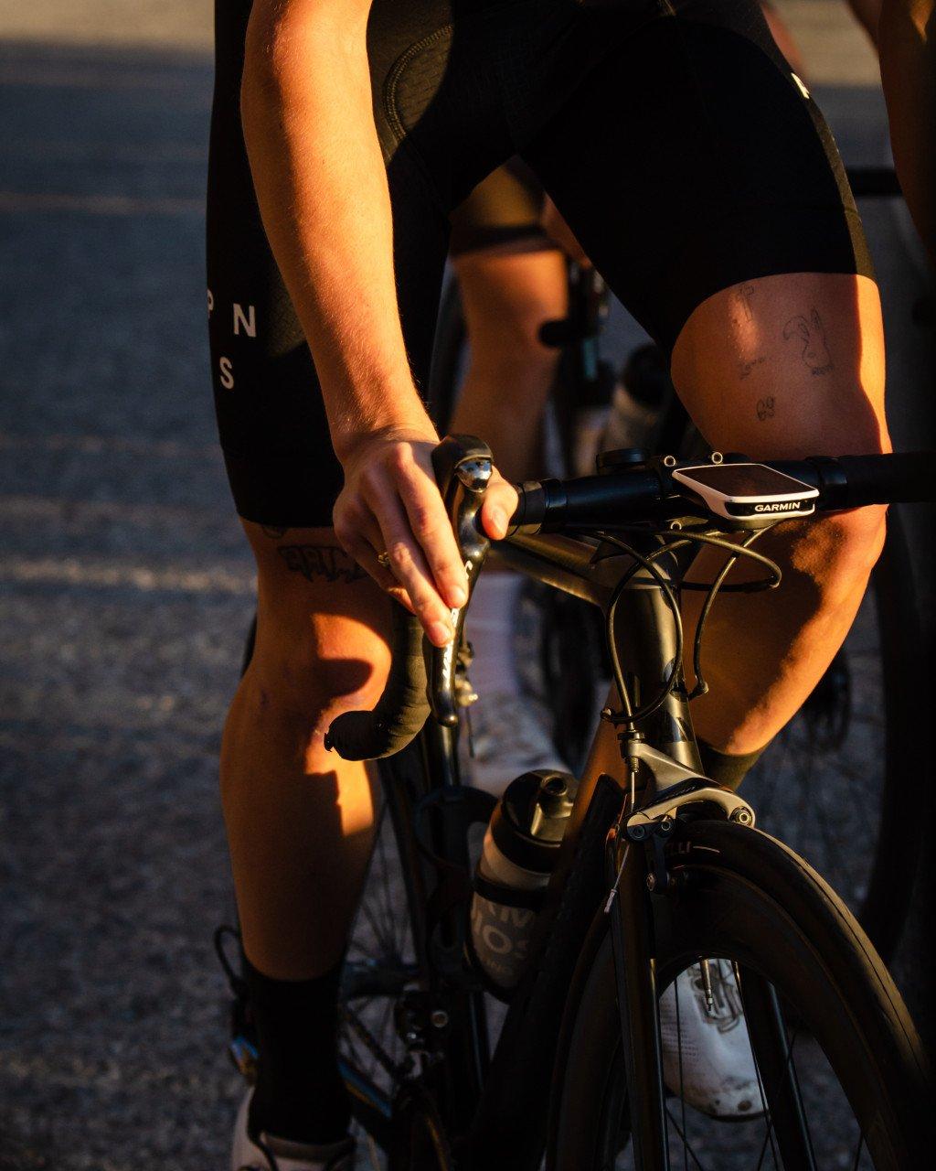 Model on time trial bike wearing black cycling kit in golden hour lighting