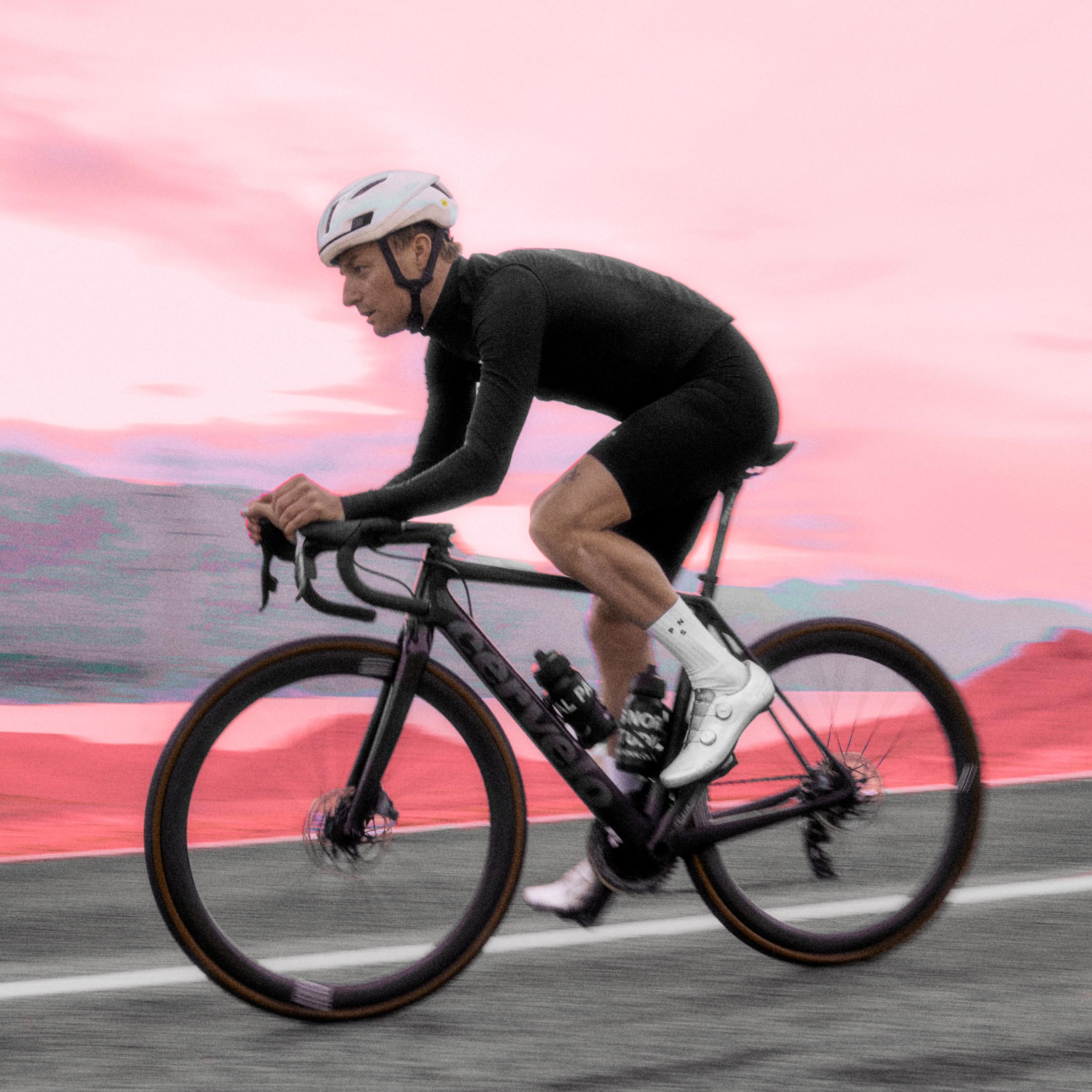 Model wearing black cycling outfit on time trial bike against pink sunset sky