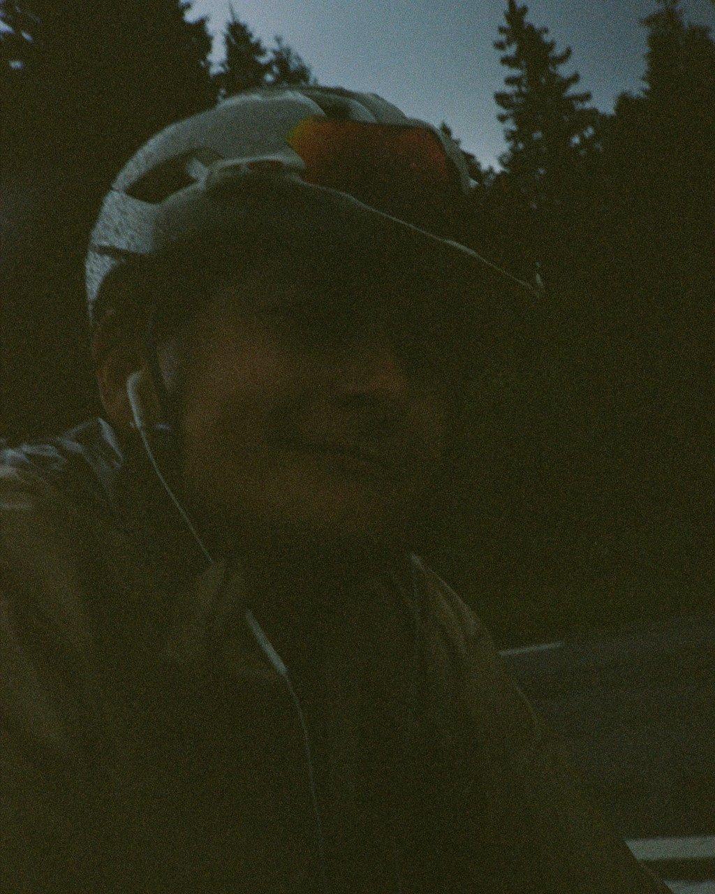 Model wearing cycling gear in low light outdoor setting with trees in background
