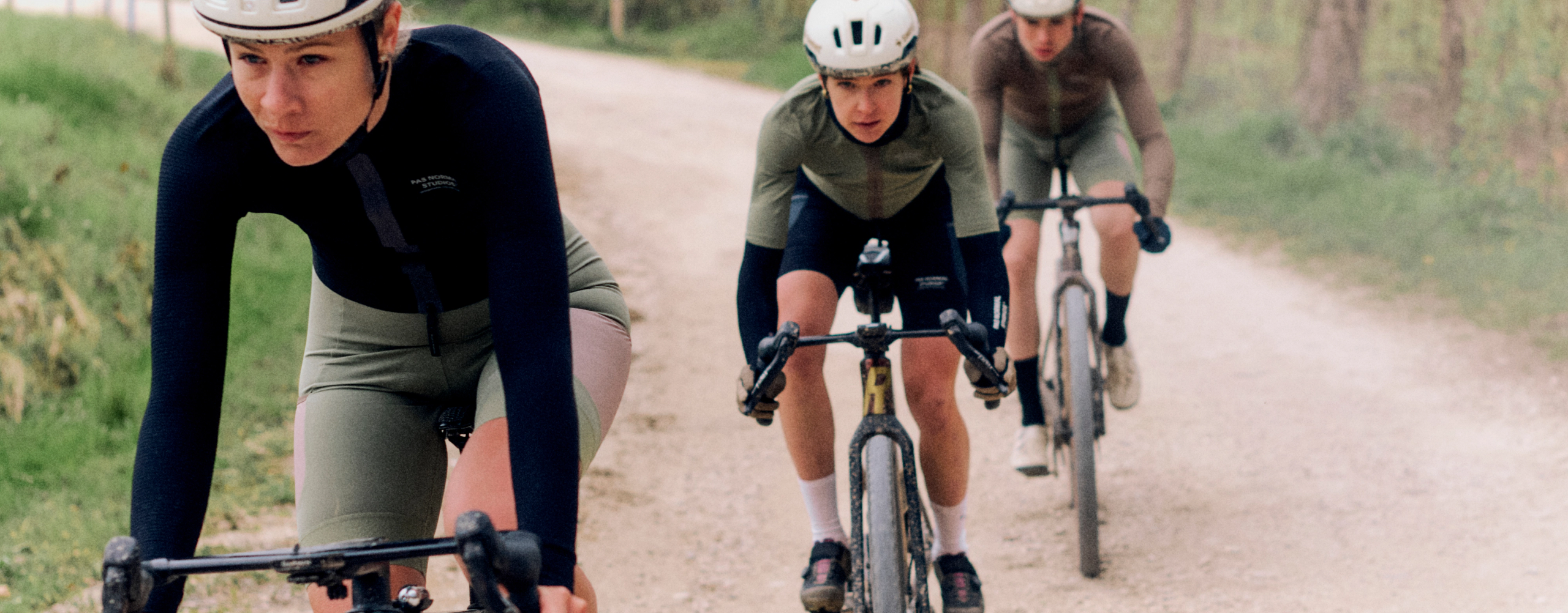 Models wearing cycling apparel in aerodynamic positions on time trial bikes on gravel road