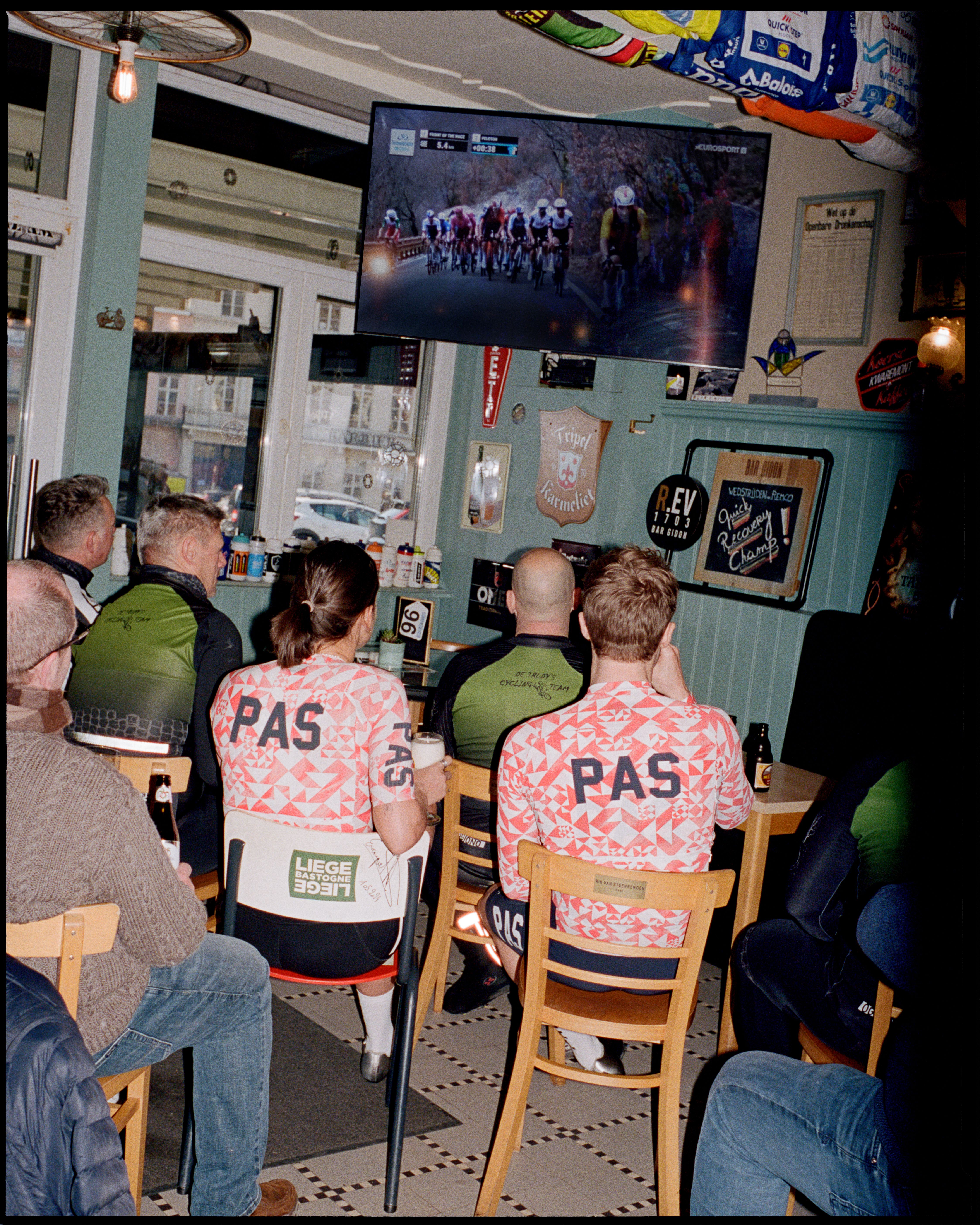 Cycling enthusiasts watching race on TV in café, wearing PAS collection jerseys with pink geometric pattern