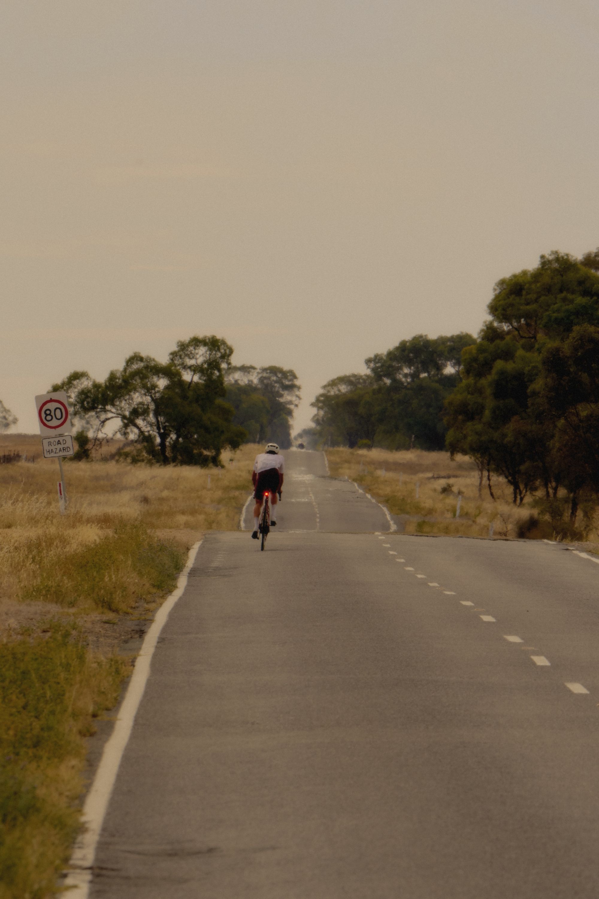 Cyclist in white jersey riding on rural road through countryside landscape