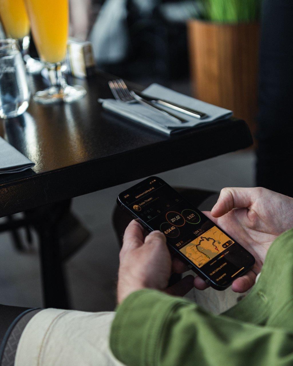 Cyclist in green top checking cycling app on phone at restaurant table with orange juice
