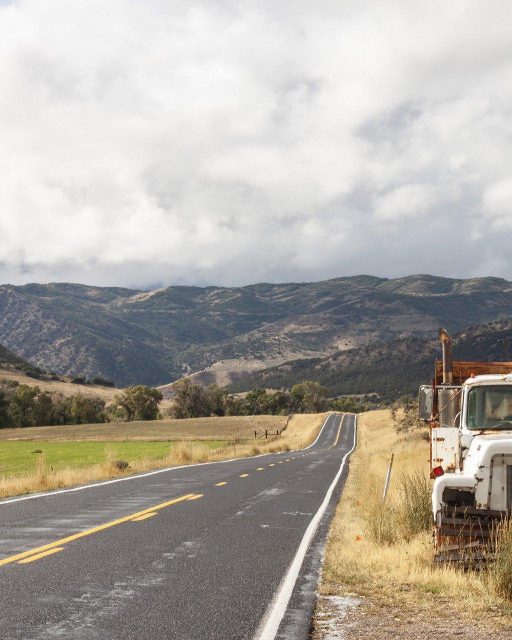 Open road stretching toward mountains under cloudy sky with truck parked on roadside