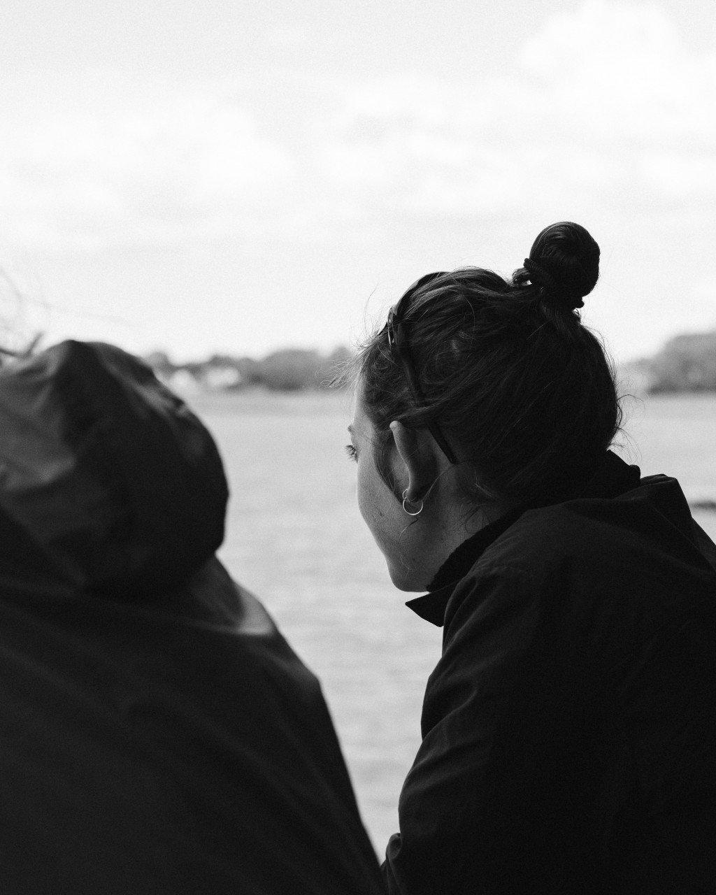 Models in dark cycling apparel photographed in profile against mountainous landscape, black and white